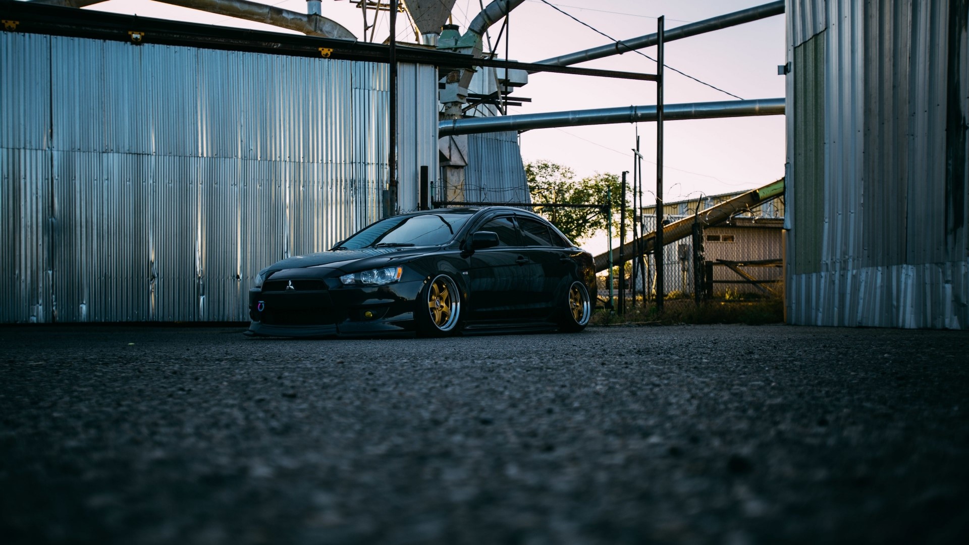 Black Mitsubishi Lancer parked near industrial buildings HD Wallpaper