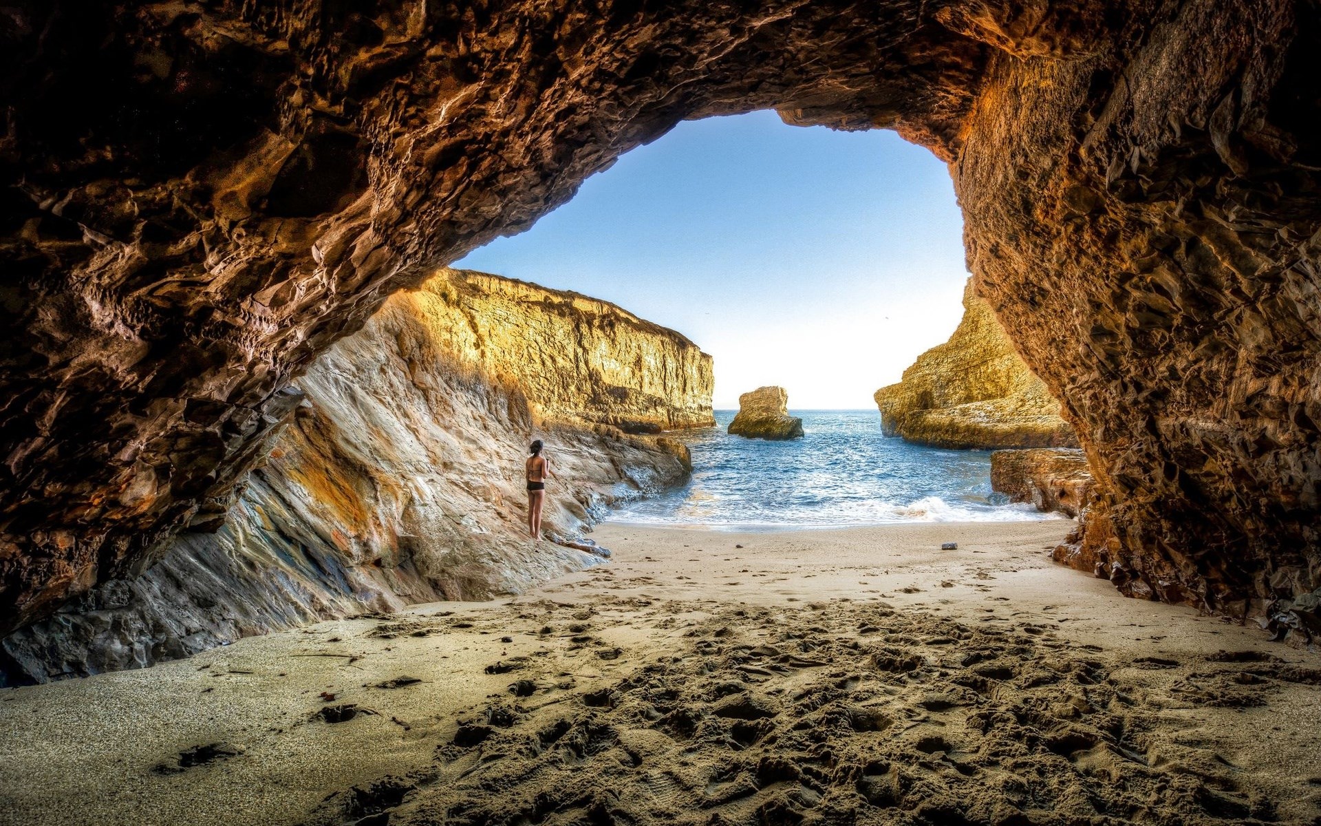 Woman standing on a beach inside a cave HD Wallpaper