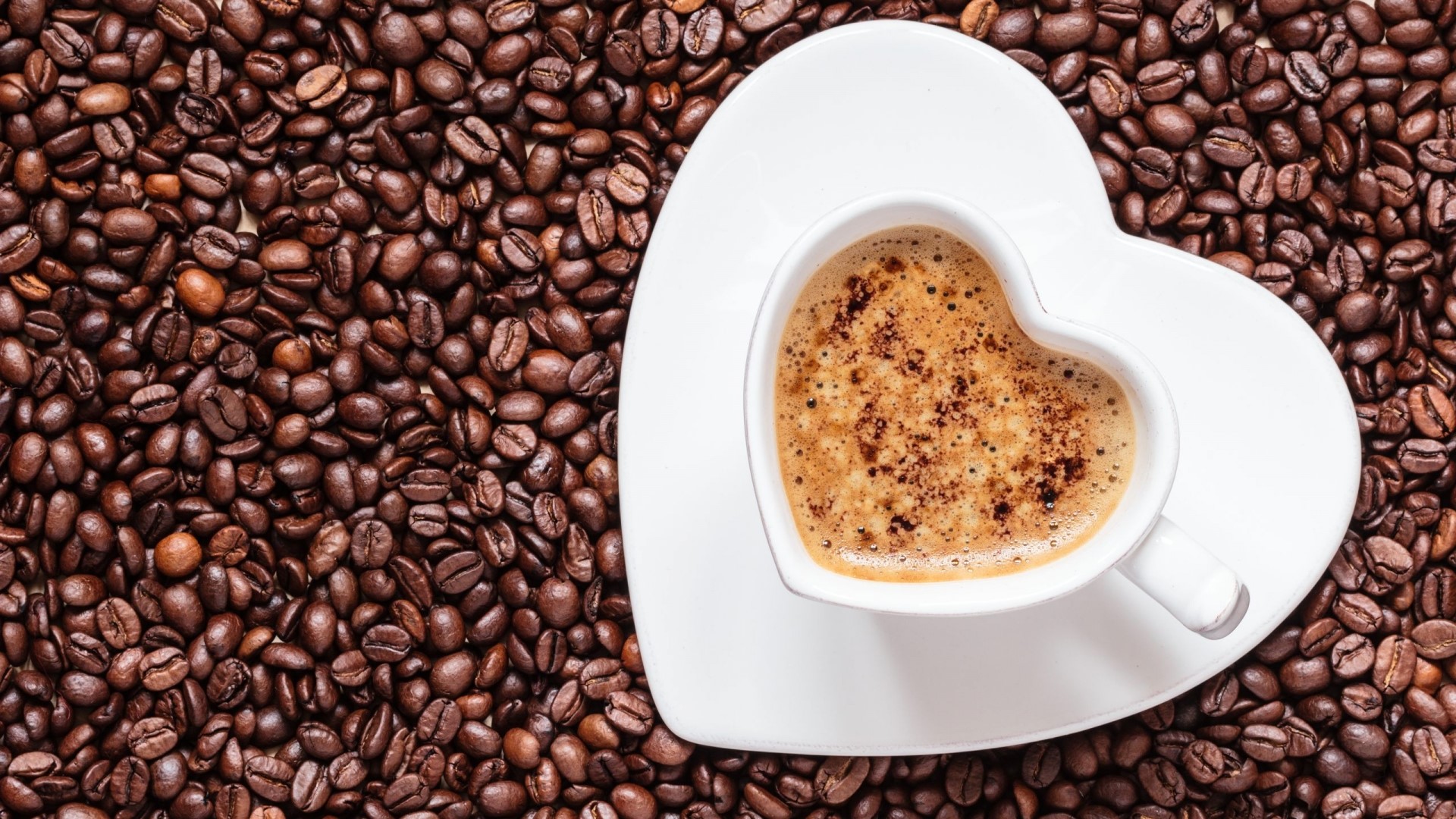 Heart-shaped cup of coffee on coffee beans HD Wallpaper