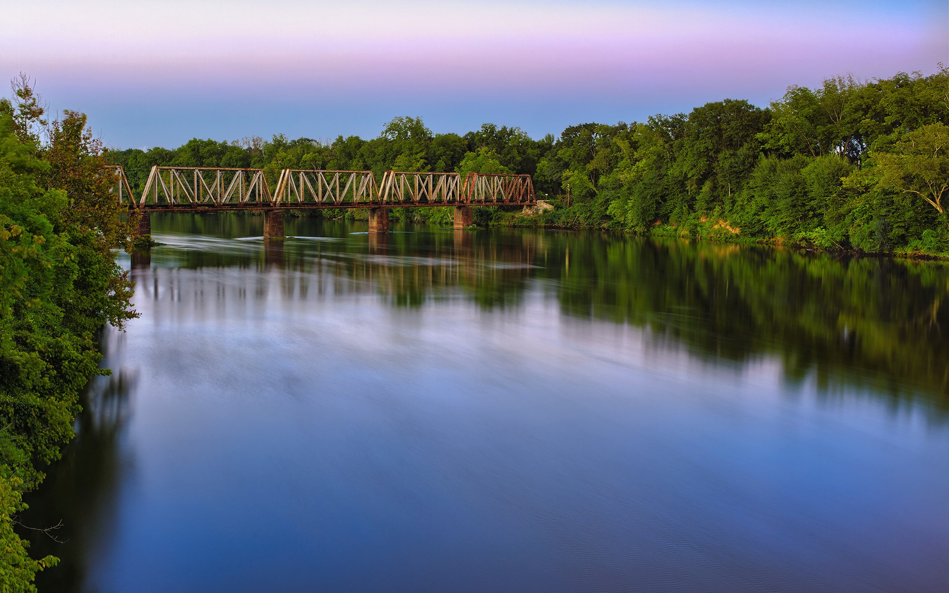 Rusty train bridge over a wide river at dusk HD Wallpaper