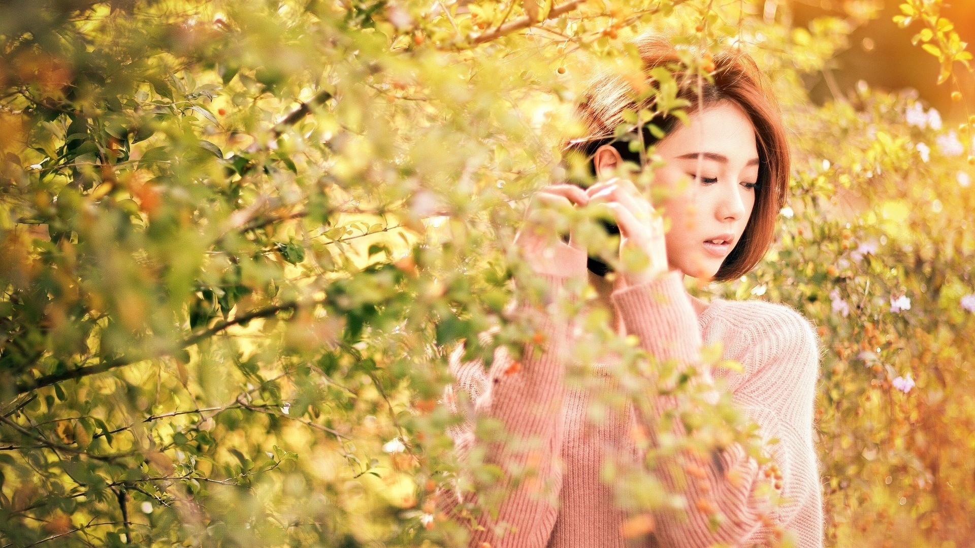 Woman in pink sweater behind foliage HD Wallpaper