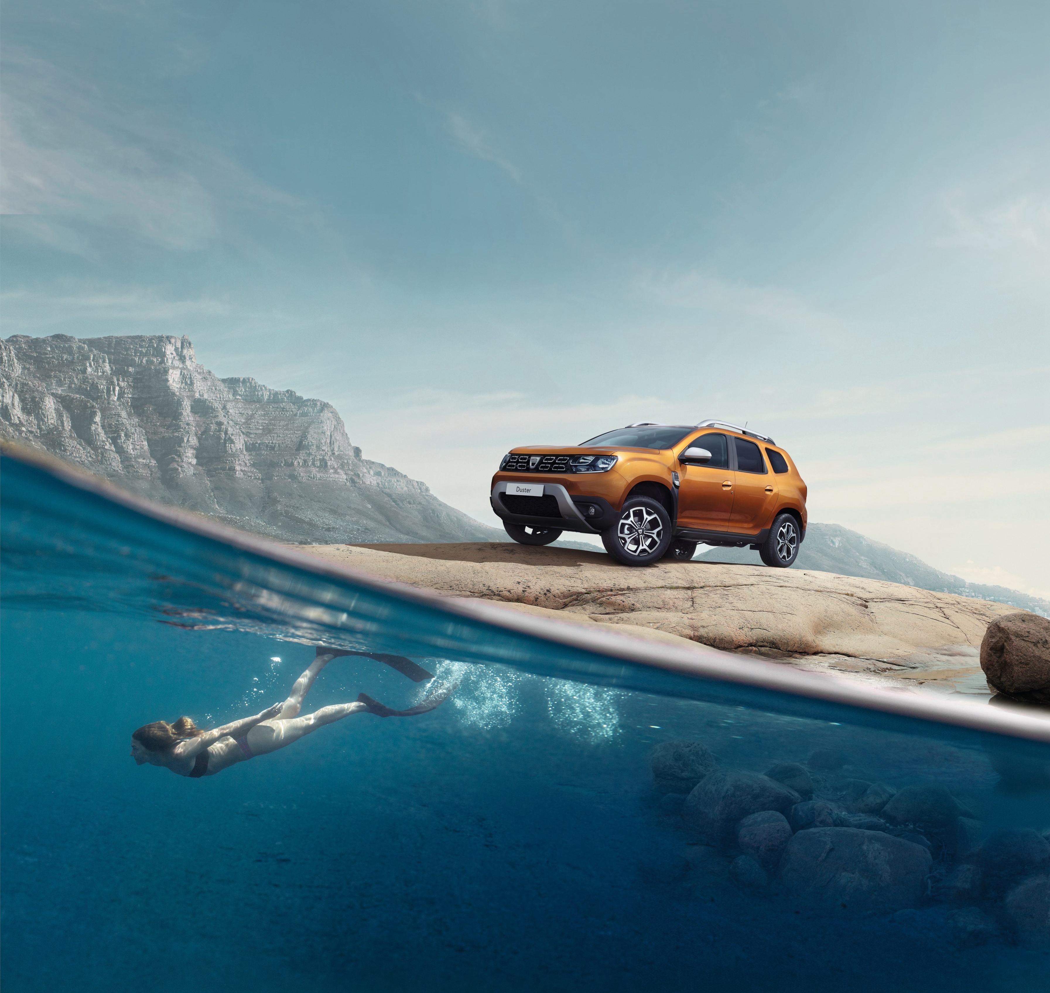 Orange Dacia Duster on rocky shore with swimmer HD Wallpaper