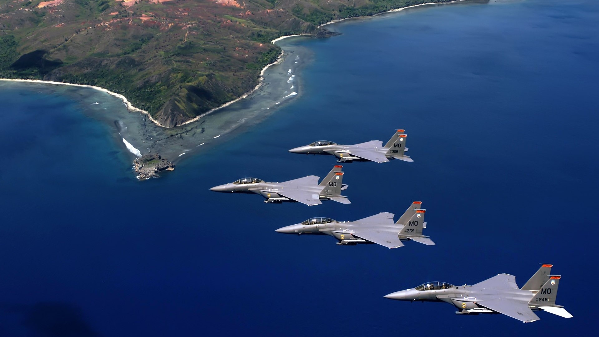 Four F-15E Strike Eagles fly over the ocean near an island HD Wallpaper