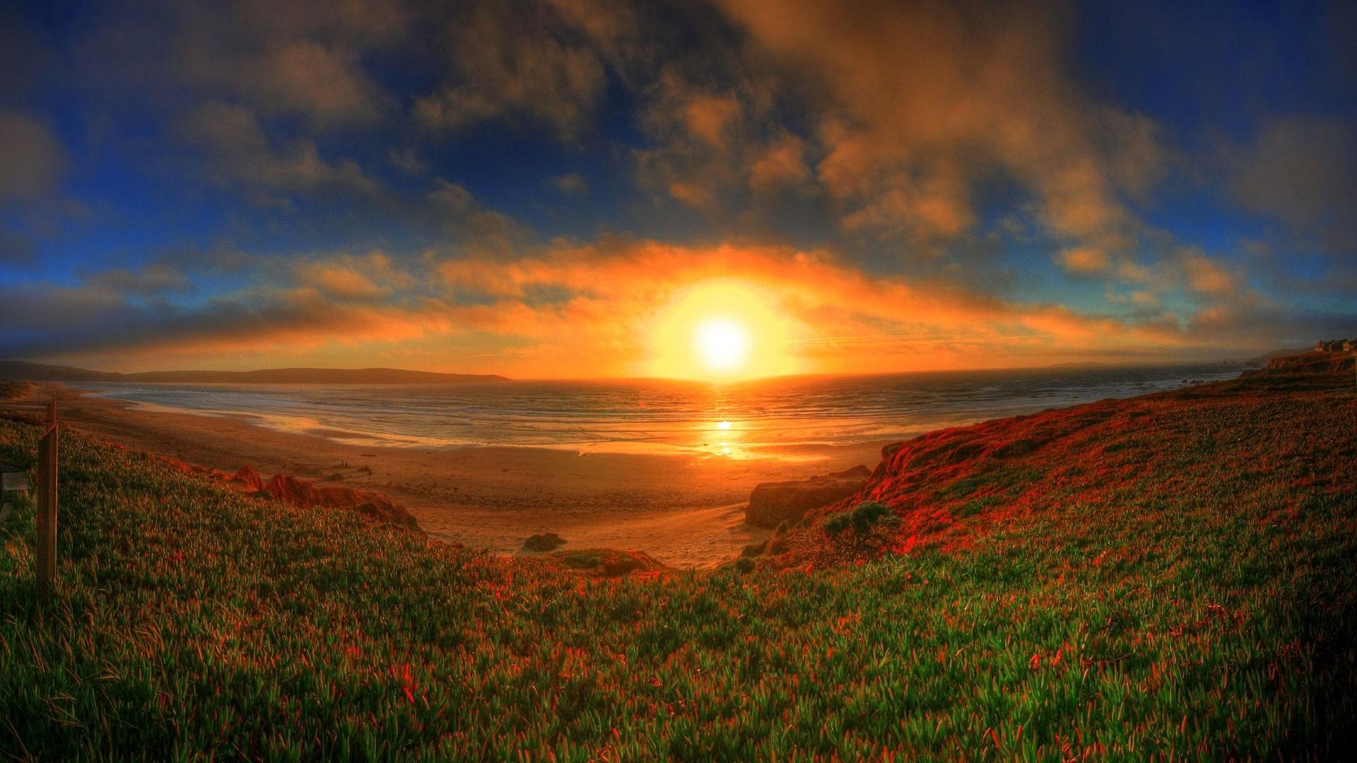 Sunset over the ocean with grassy hills HD Wallpaper