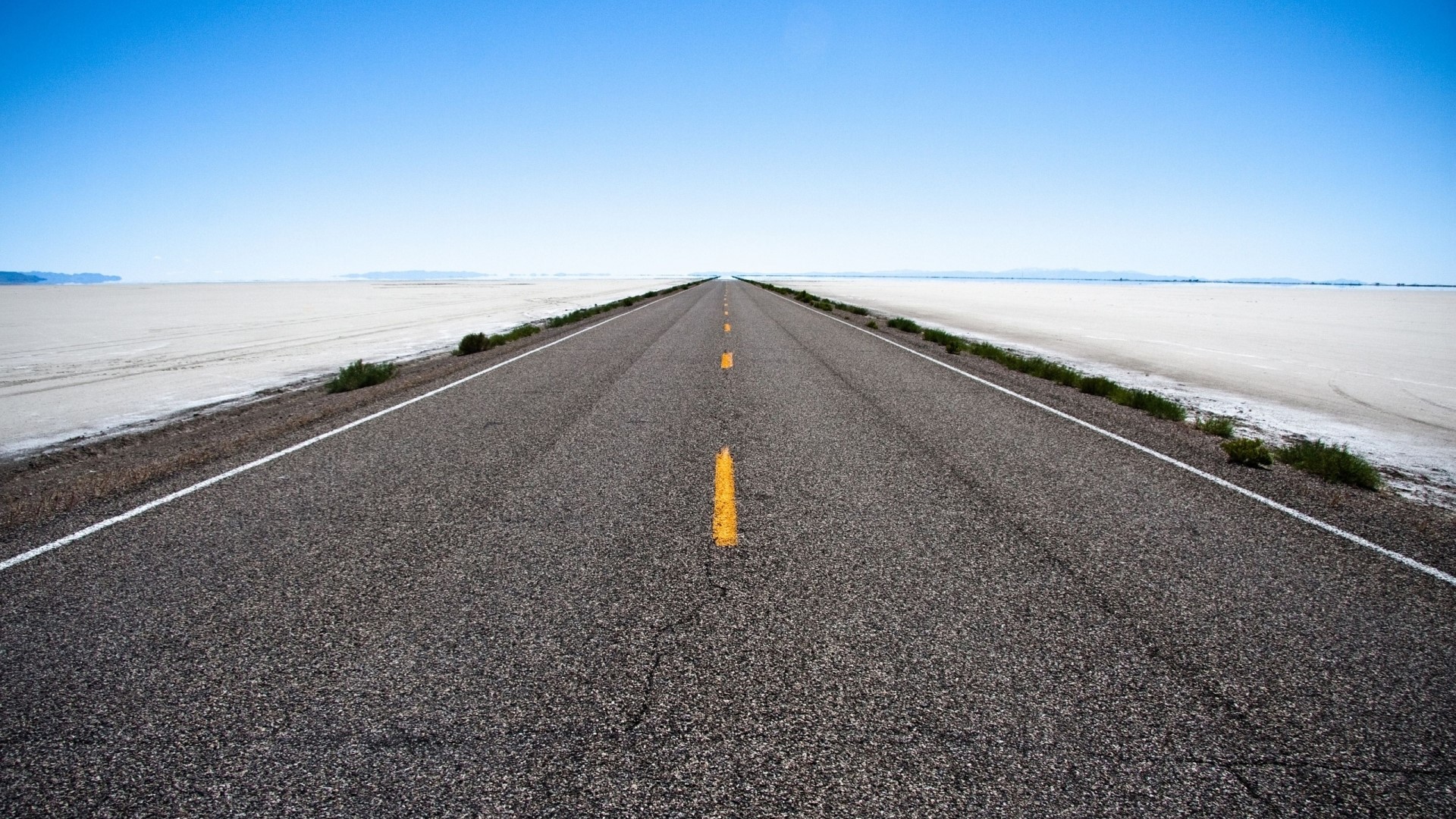 Endless road stretching to the horizon under a clear blue sky HD Wallpaper