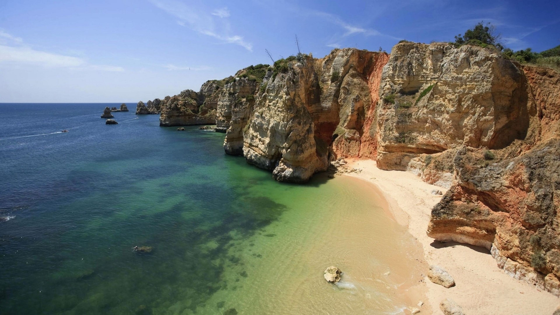 Rocky coastline with a sandy beach and clear blue water HD Wallpaper