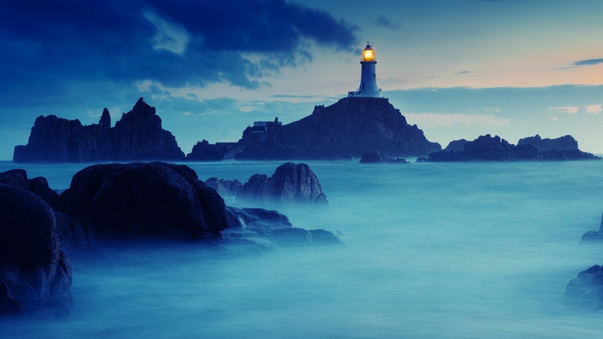 Lighthouse on a rocky island at dusk HD Wallpaper