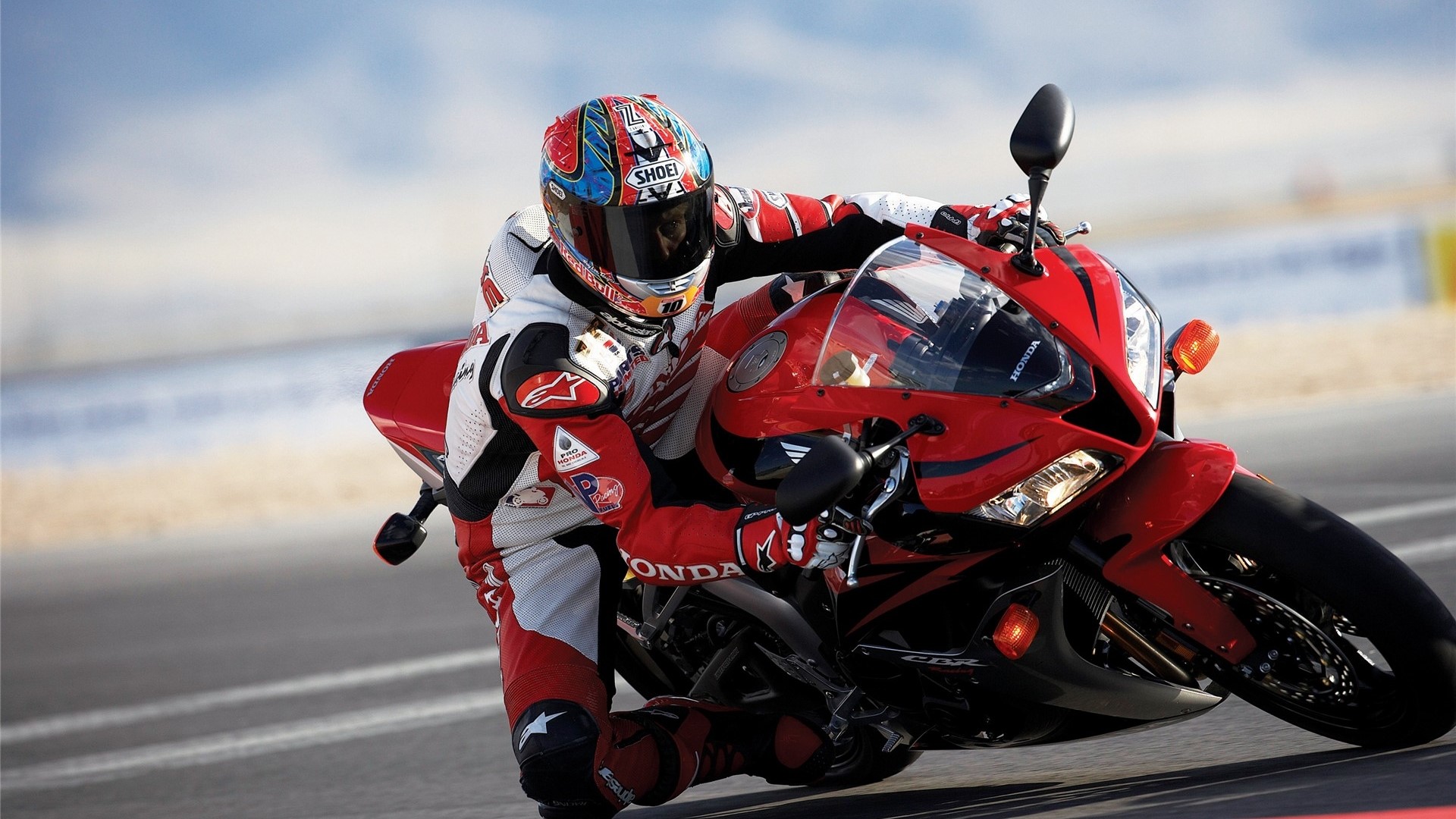 Motorcyclist in red and white racing suit on a red Honda CBR motorcycle HD Wallpaper