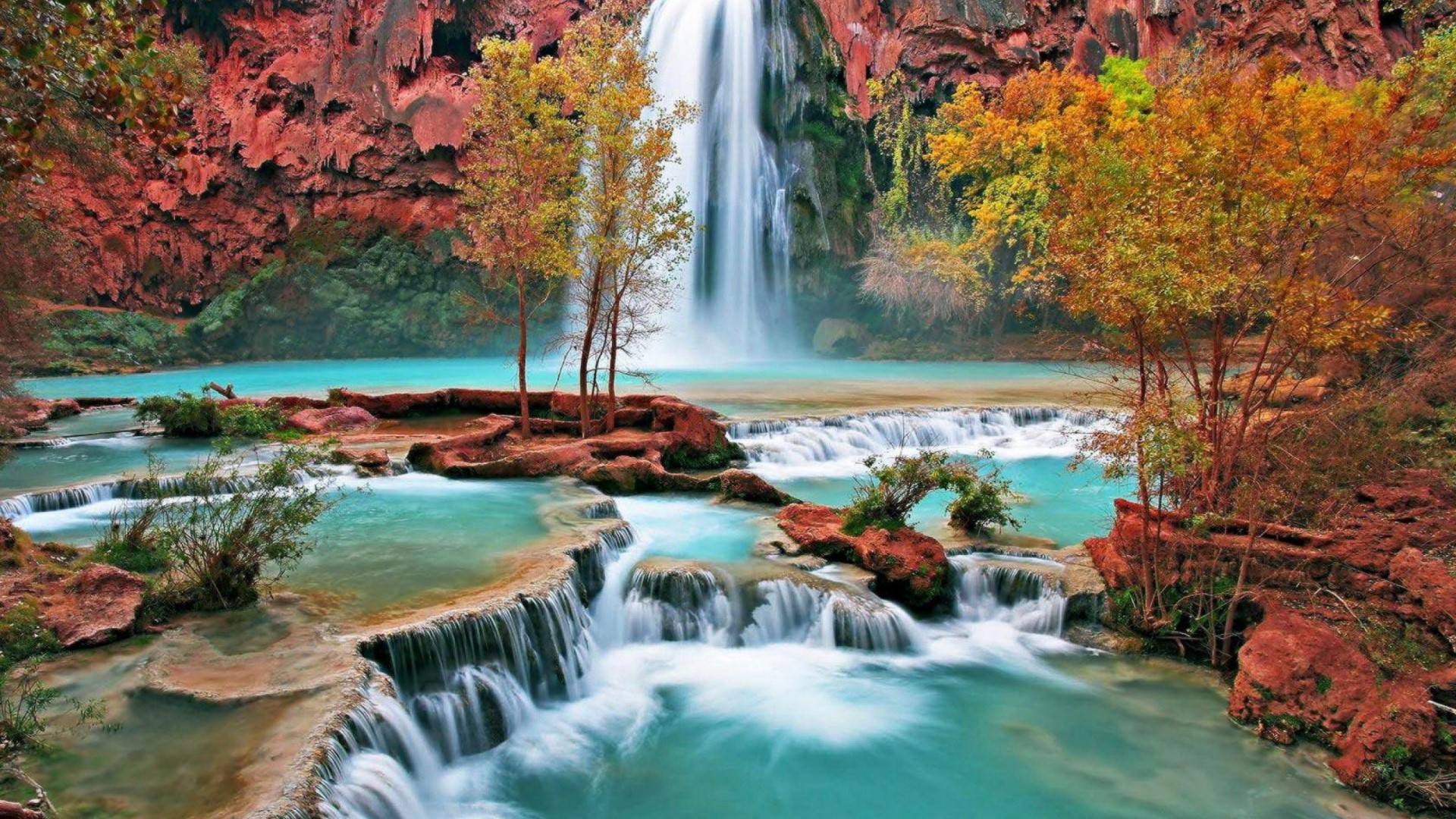 Turquoise waterfall cascading over red rocks with autumn trees HD Wallpaper