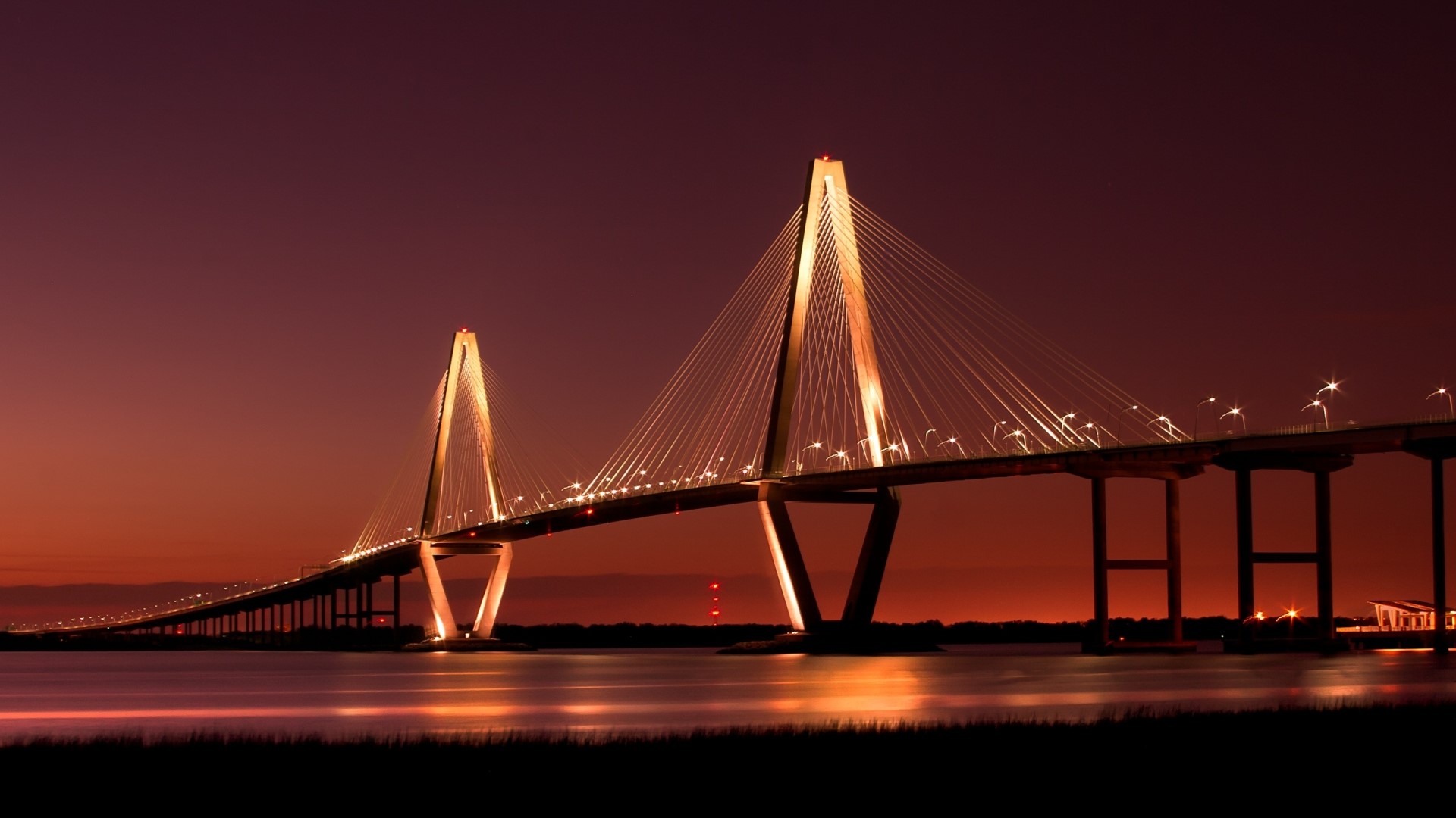 Cable-stayed bridge illuminated at dusk over water HD Wallpaper