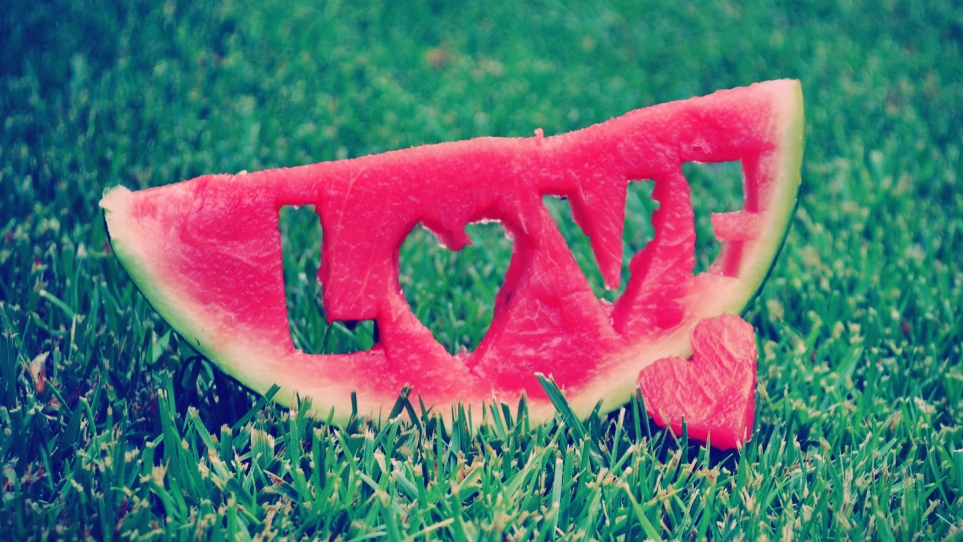 Watermelon slice with 'LOVE' carved out on grass HD Wallpaper