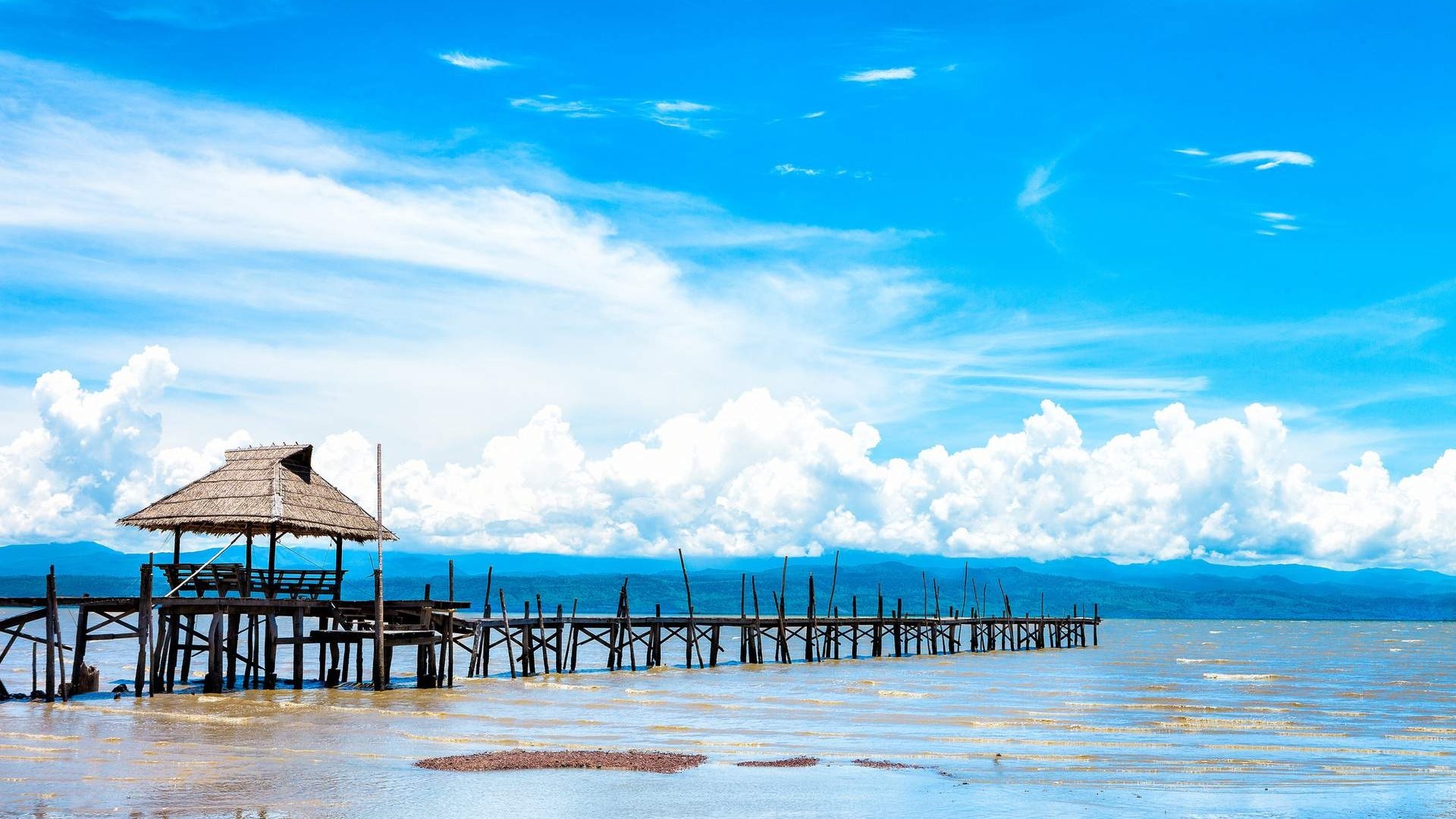 Wooden pier with thatched hut on a lake under blue sky HD Wallpaper