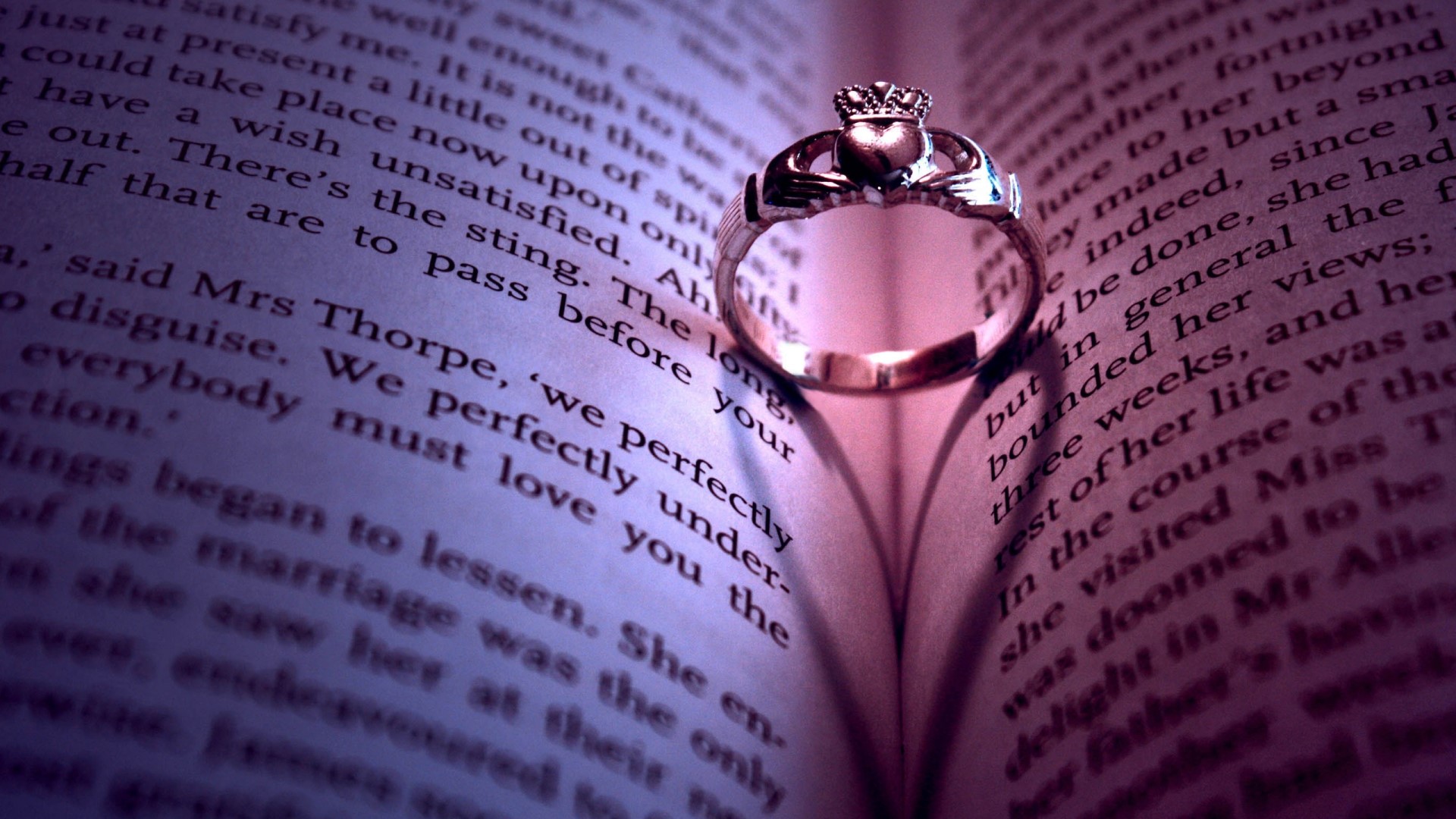 Claddagh ring casting a heart shadow on an open book HD Wallpaper