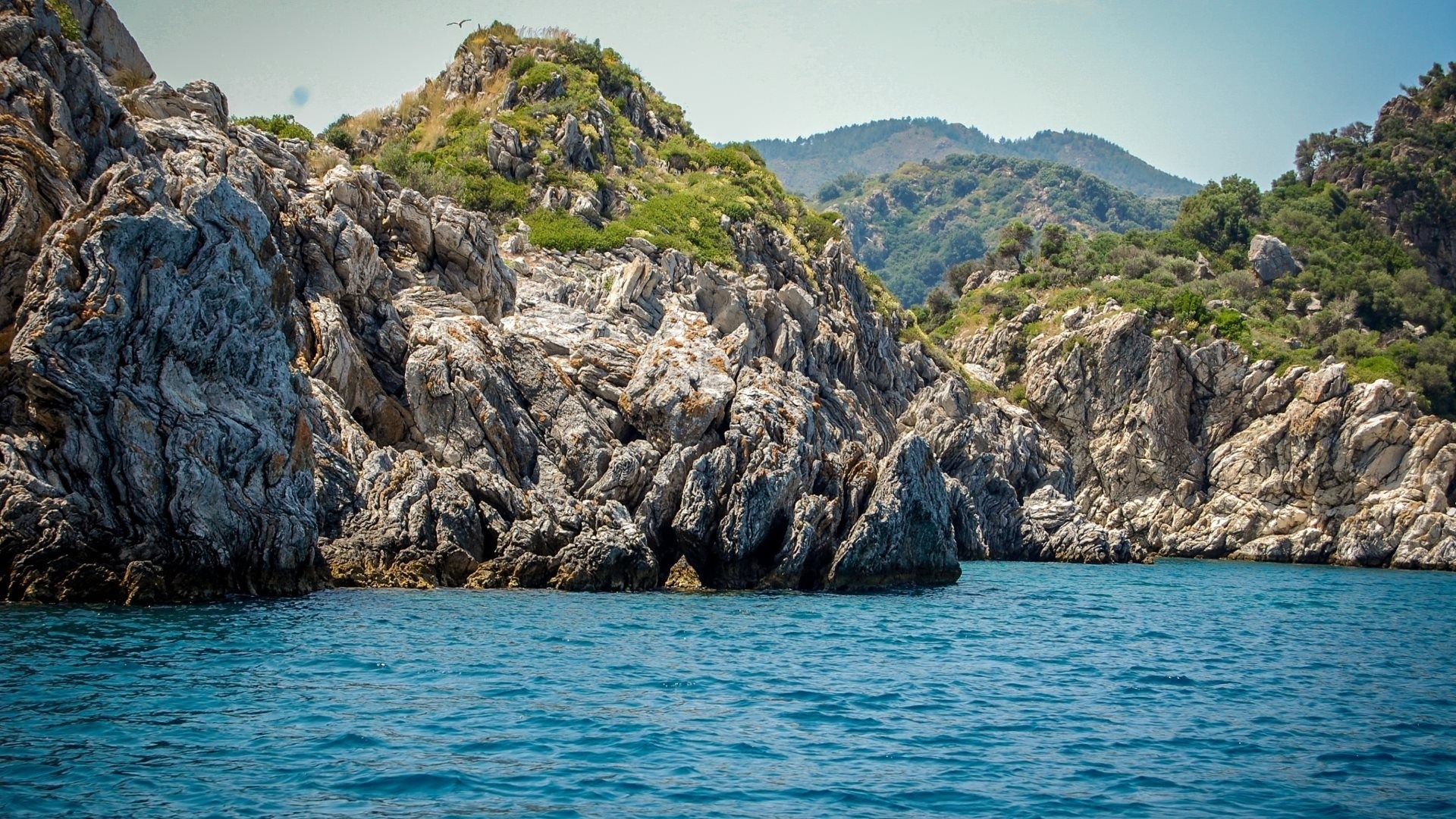 Rocky coastline with green mountains and blue sea HD Wallpaper