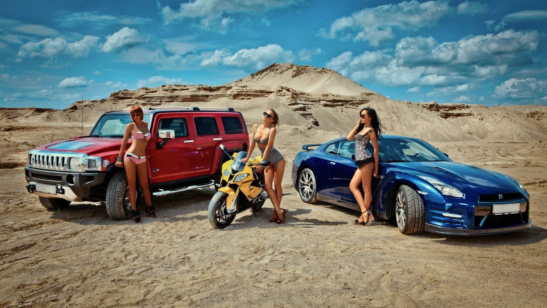 Three women with a red SUV, yellow motorcycle, and blue sports car in the desert. HD Wallpaper