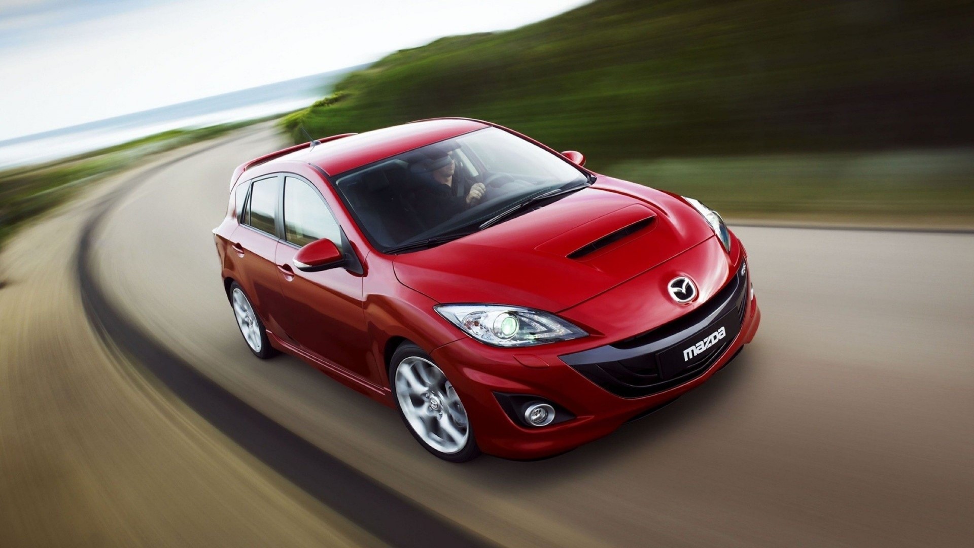 Red Mazda 3 MPS driving on a coastal road HD Wallpaper