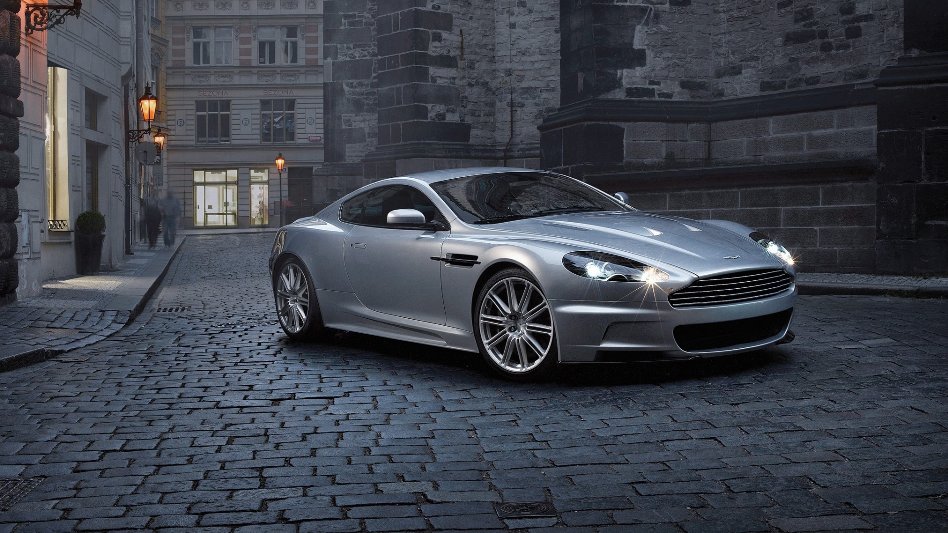 Silver Aston Martin DBS parked on cobblestone street HD Wallpaper