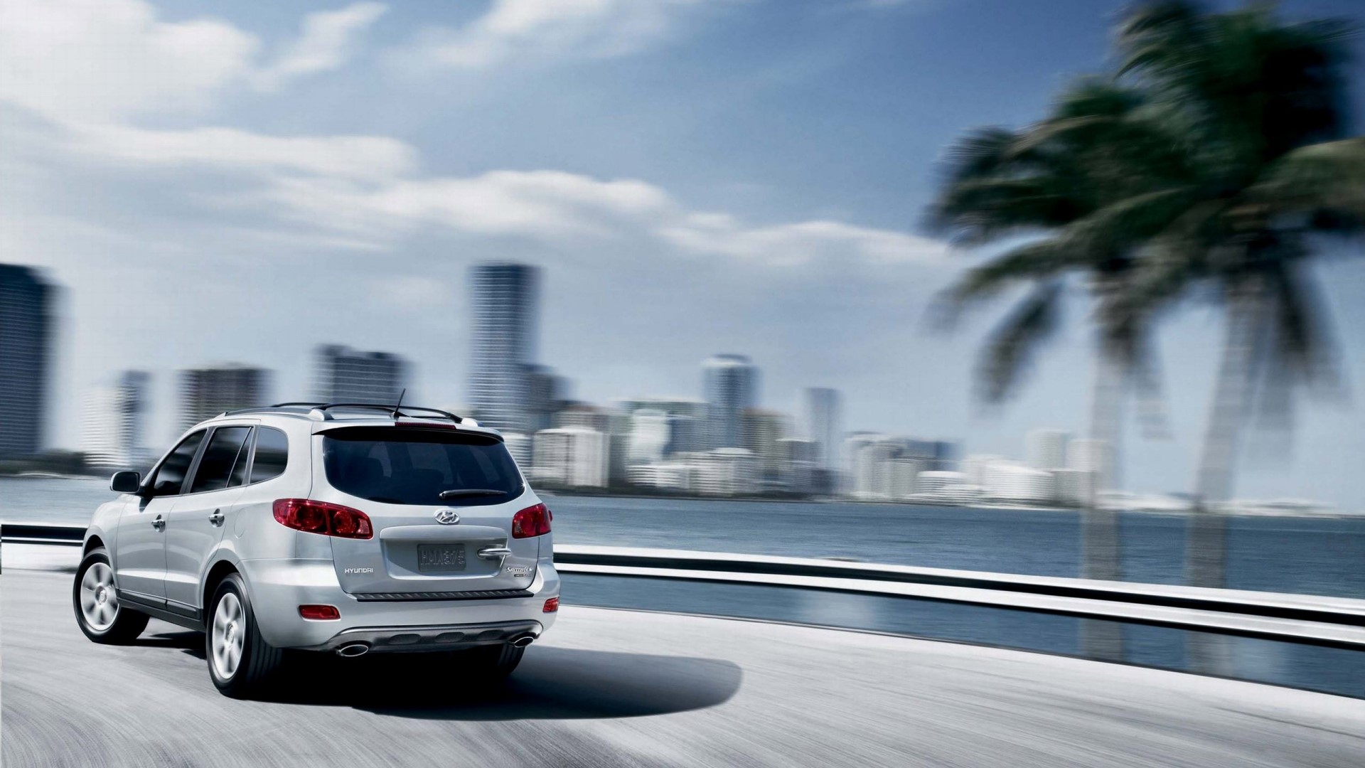 Silver Hyundai Santa Fe SUV driving by a city skyline HD Wallpaper