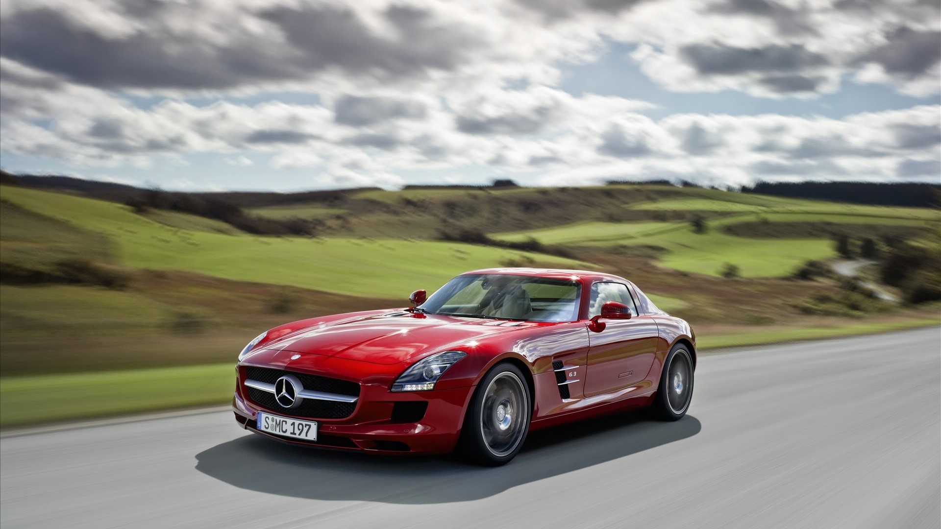 Red Mercedes-Benz SLS AMG driving on a road HD Wallpaper