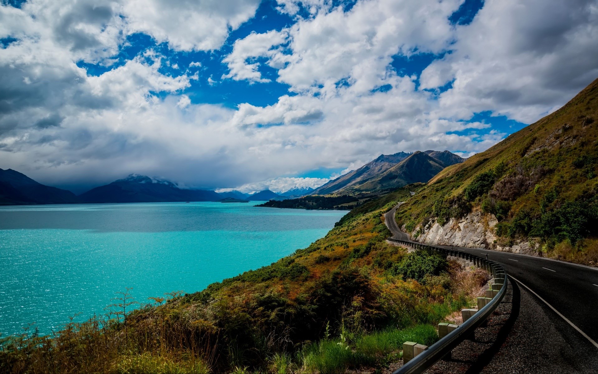 Winding road along a turquoise lake and mountains HD Wallpaper