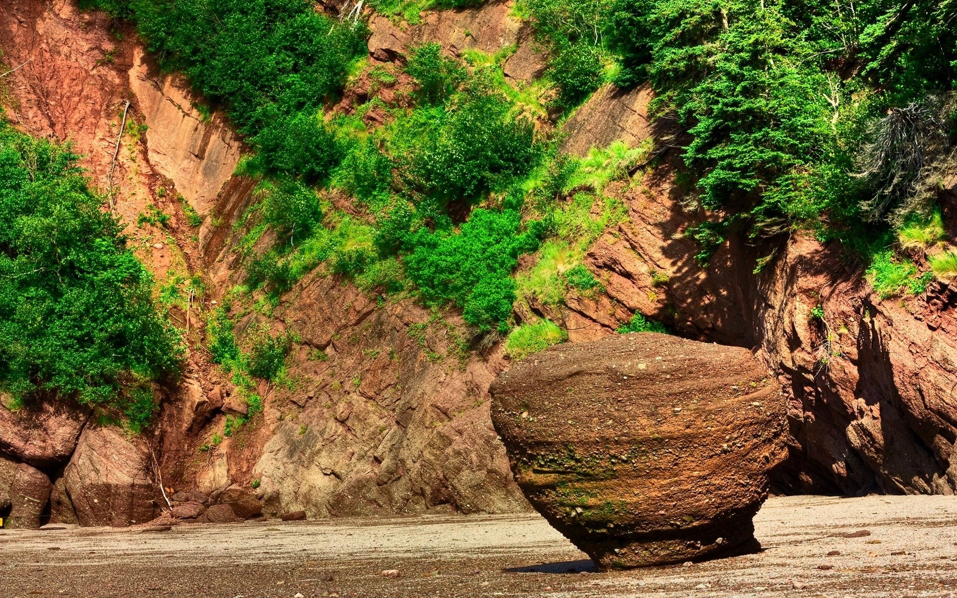 Boulder on a beach with red cliffs and green foliage HD Wallpaper