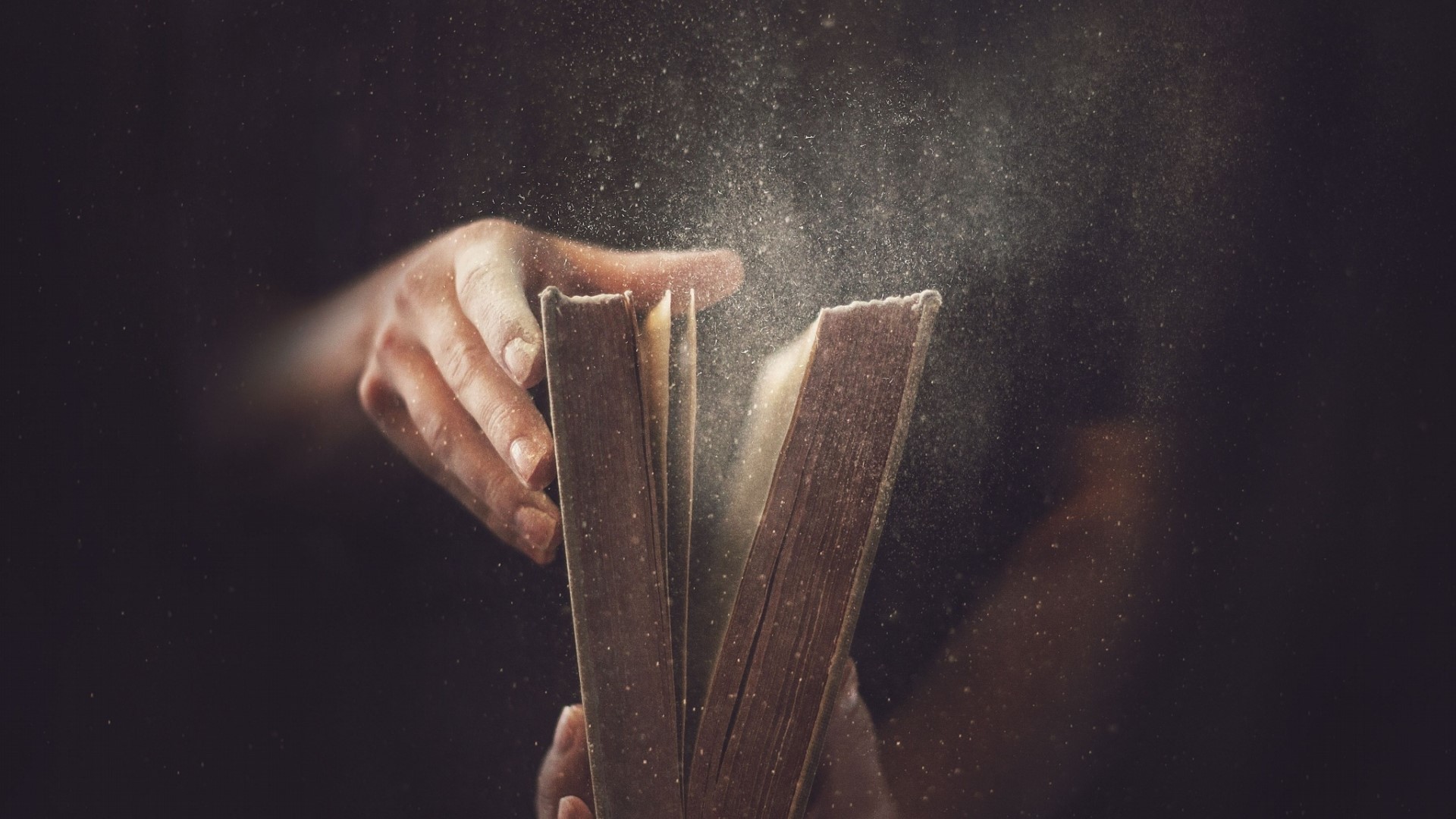 Hands opening an old book with dust flying HD Wallpaper