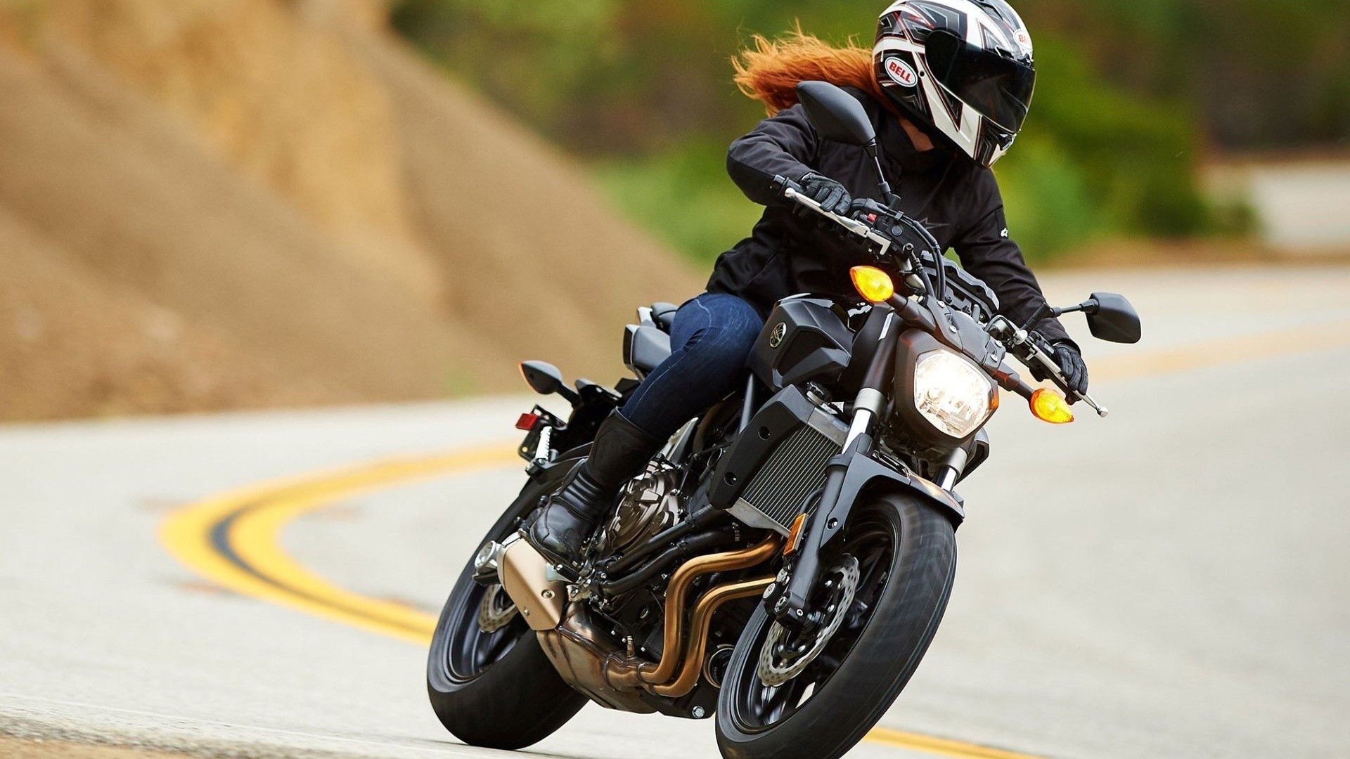 Woman riding a Yamaha FZ-07 motorcycle on a winding road HD Wallpaper