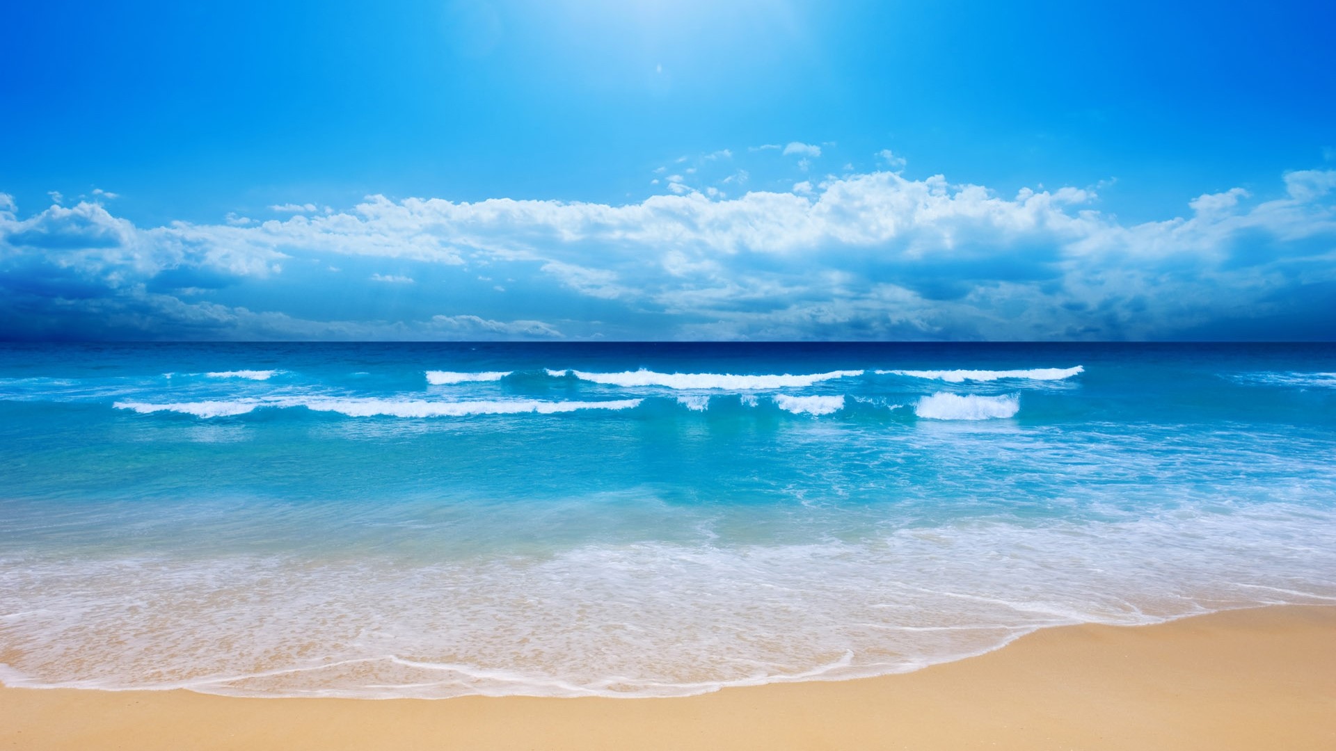 Ocean waves on a sandy beach under a blue sky HD Wallpaper