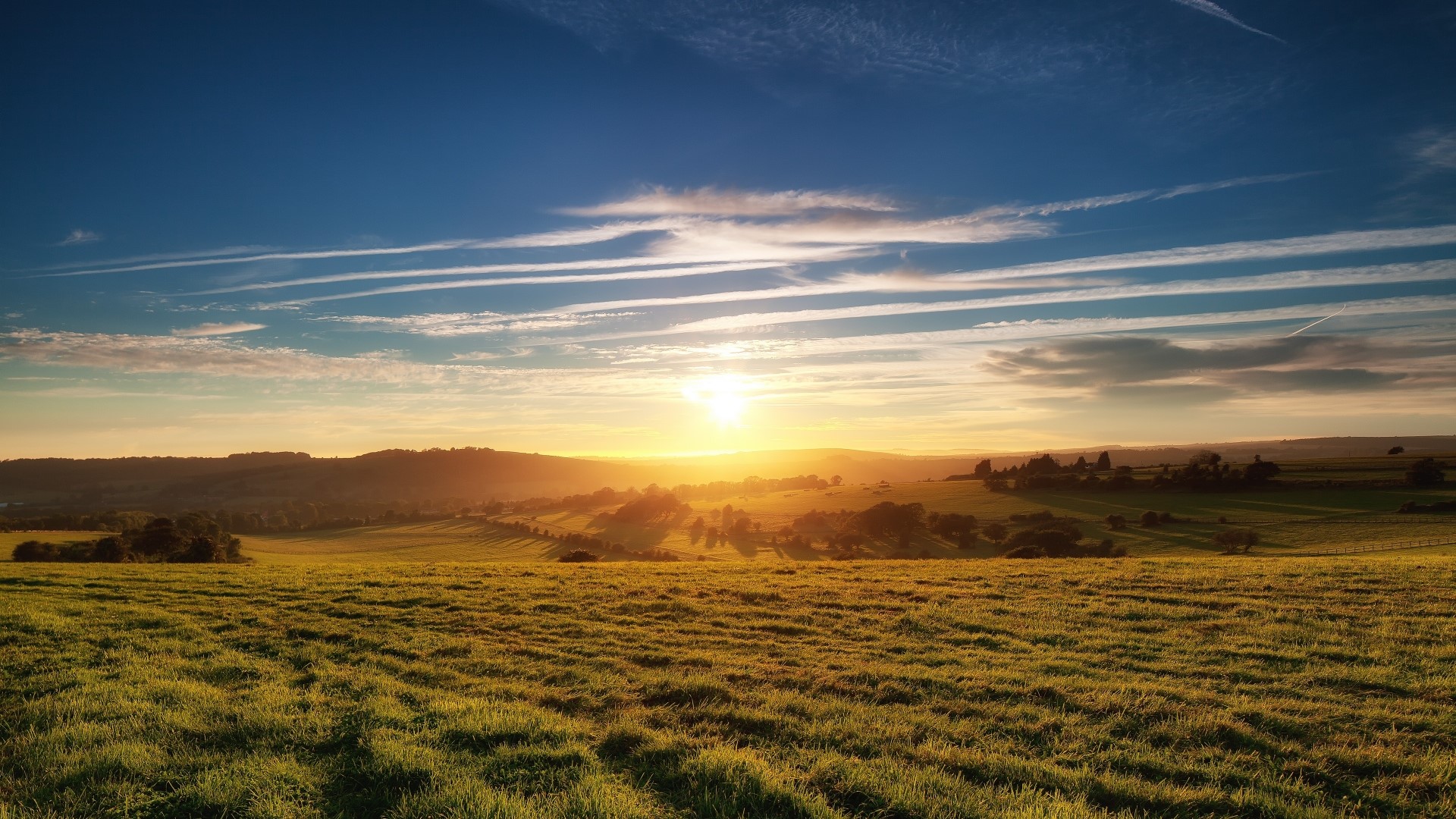 Sun rising over rolling green hills HD Wallpaper