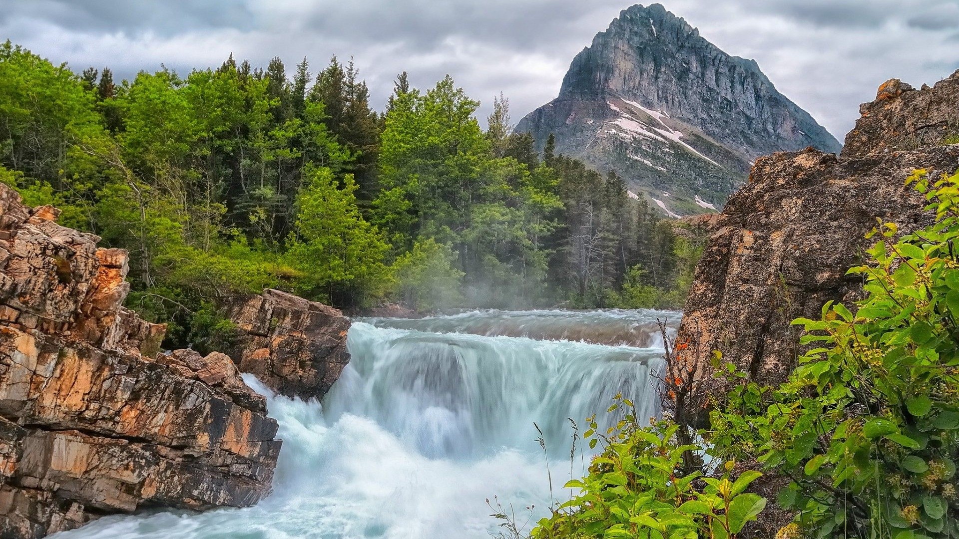 Waterfall flowing through rocks with mountain and trees in background HD Wallpaper