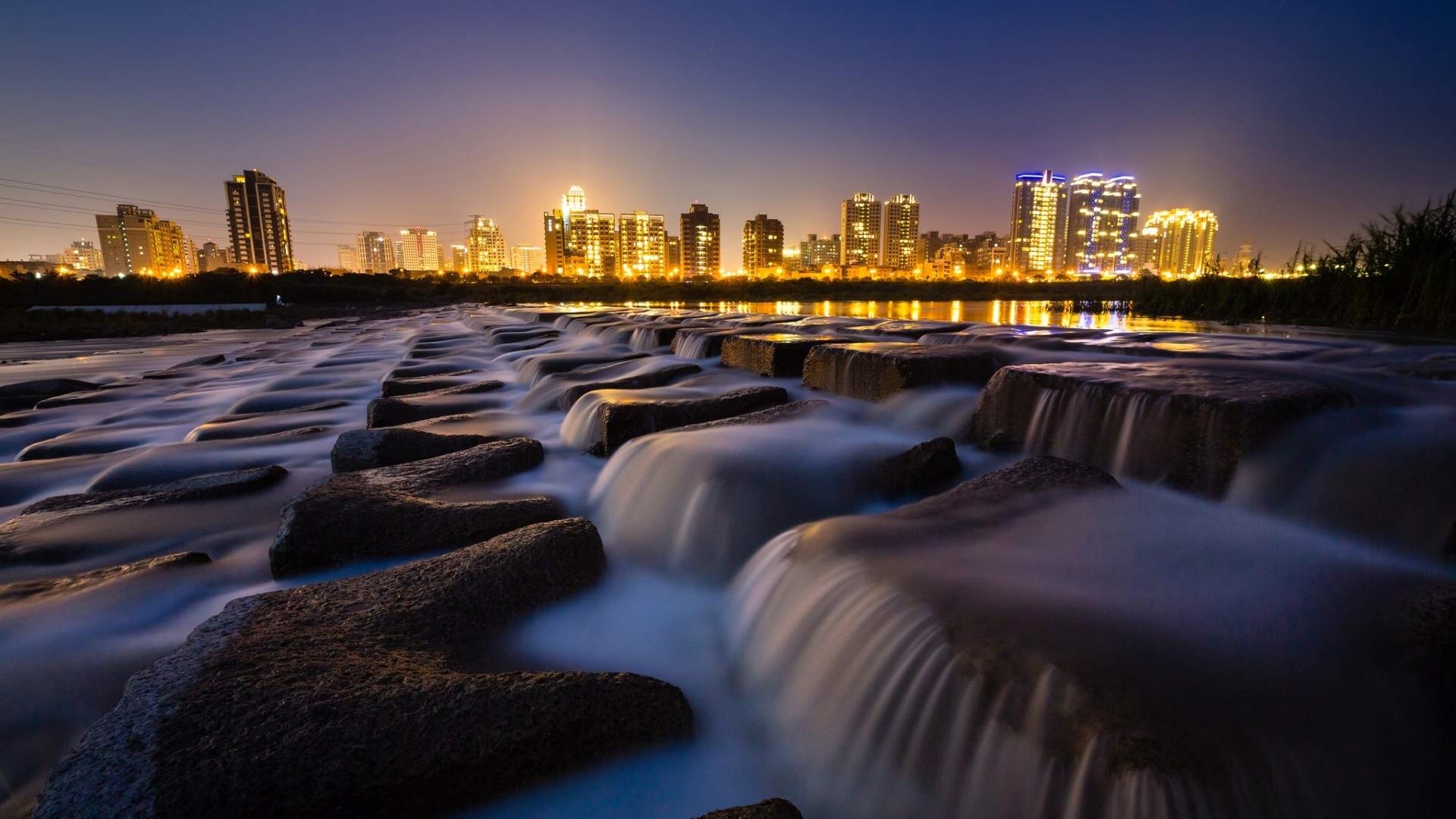 Cityscape at Night with Water Flowing Over Rocks HD Wallpaper