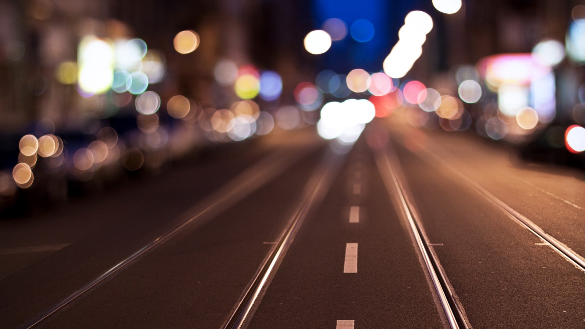 Tram lines on a city street at night with bokeh lights HD Wallpaper
