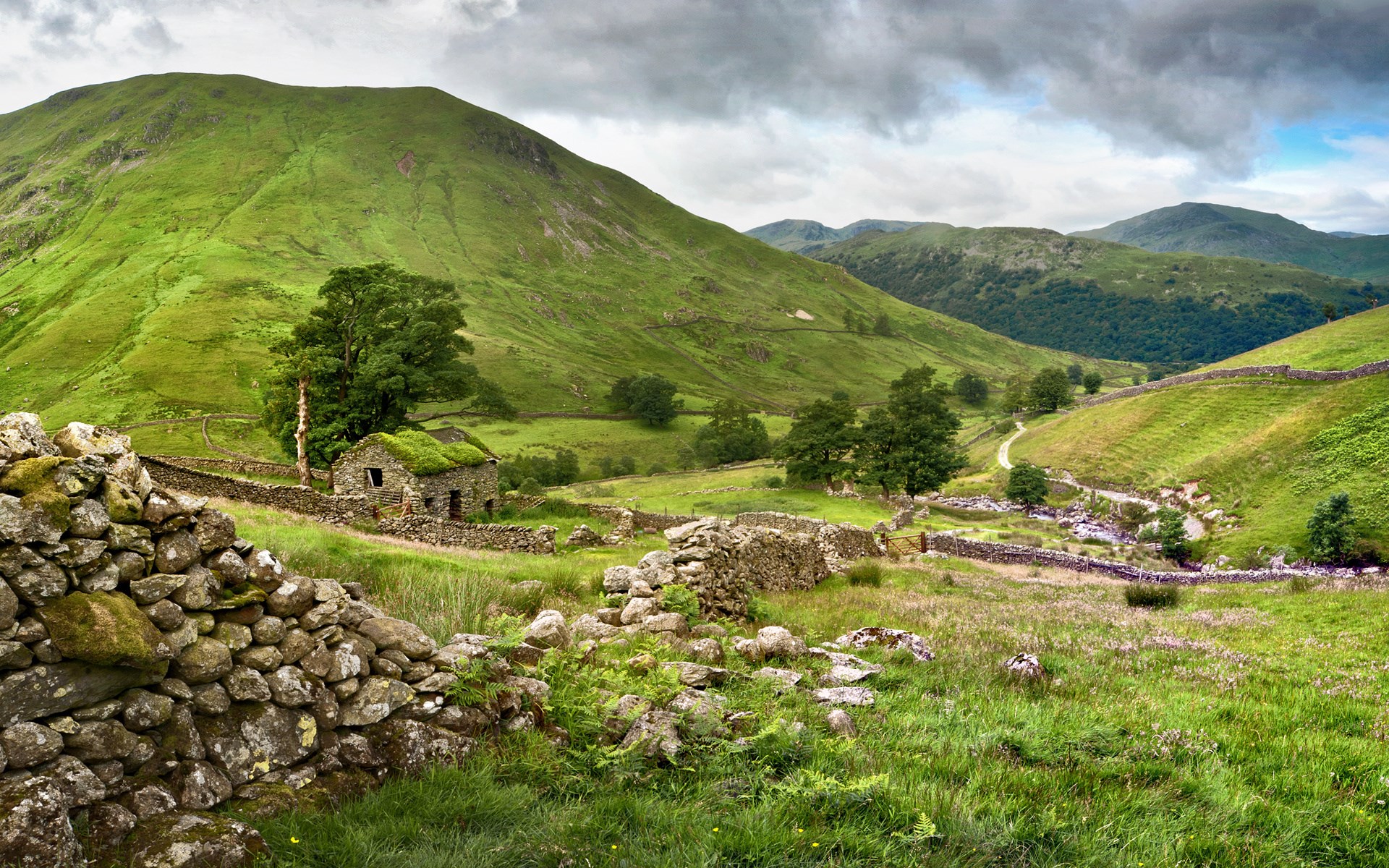 Stone cottage in a green valley with rolling hills HD Wallpaper