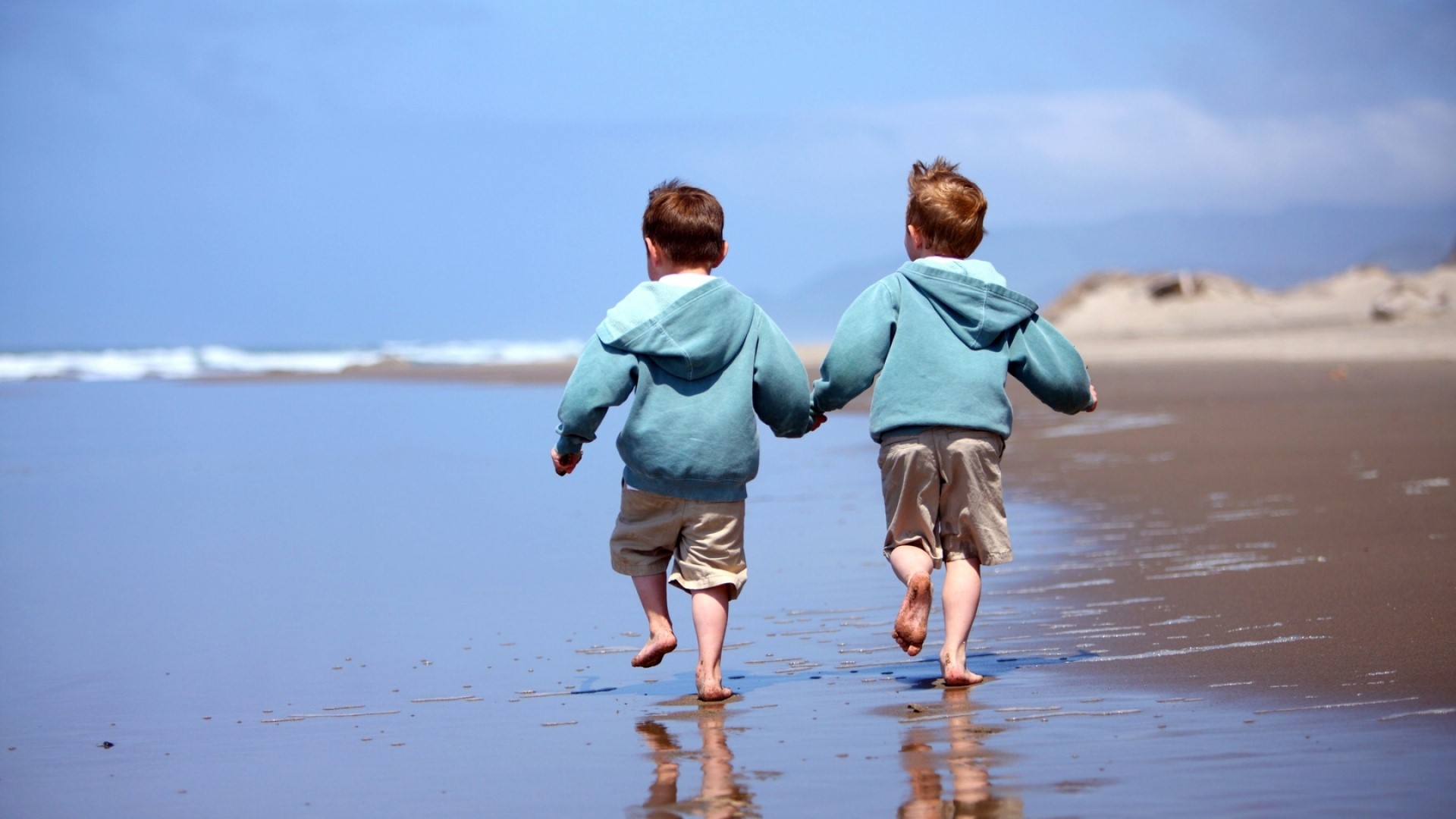 Two young boys holding hands on a beach HD Wallpaper