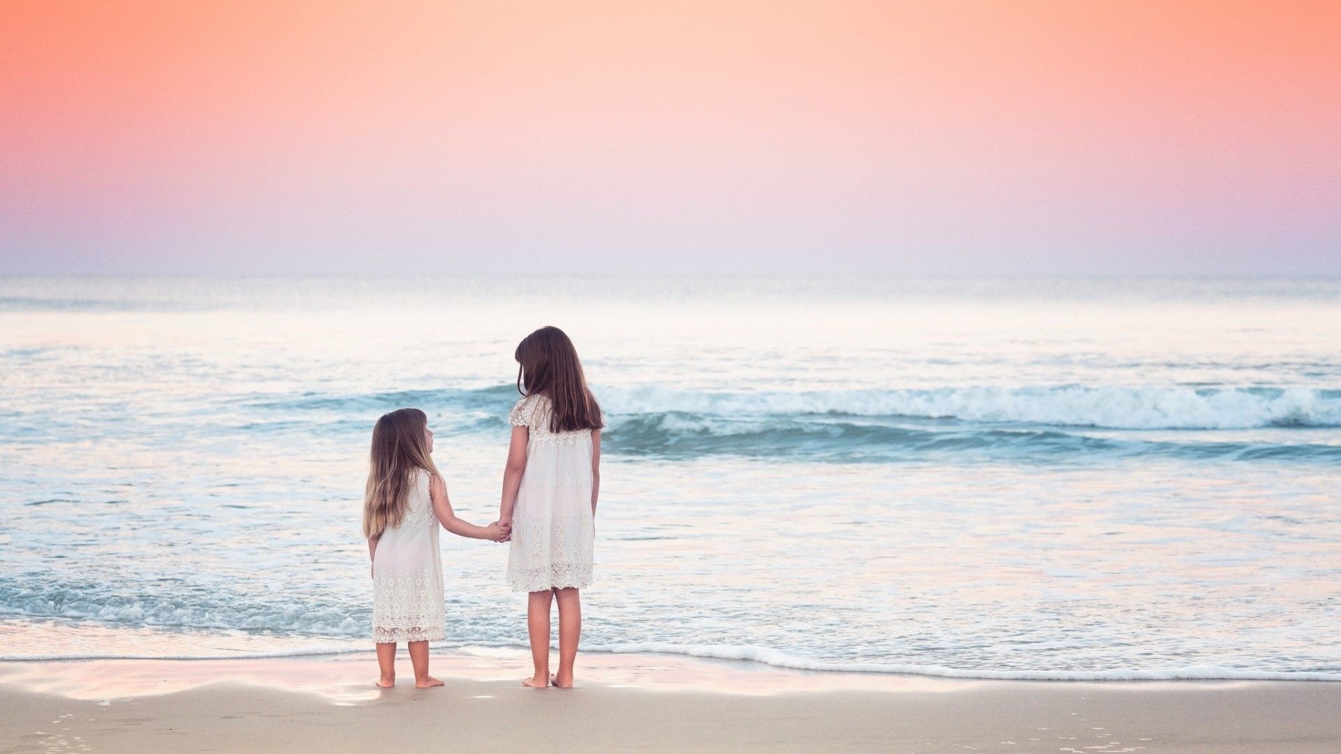 Two young girls holding hands on a beach at sunset HD Wallpaper