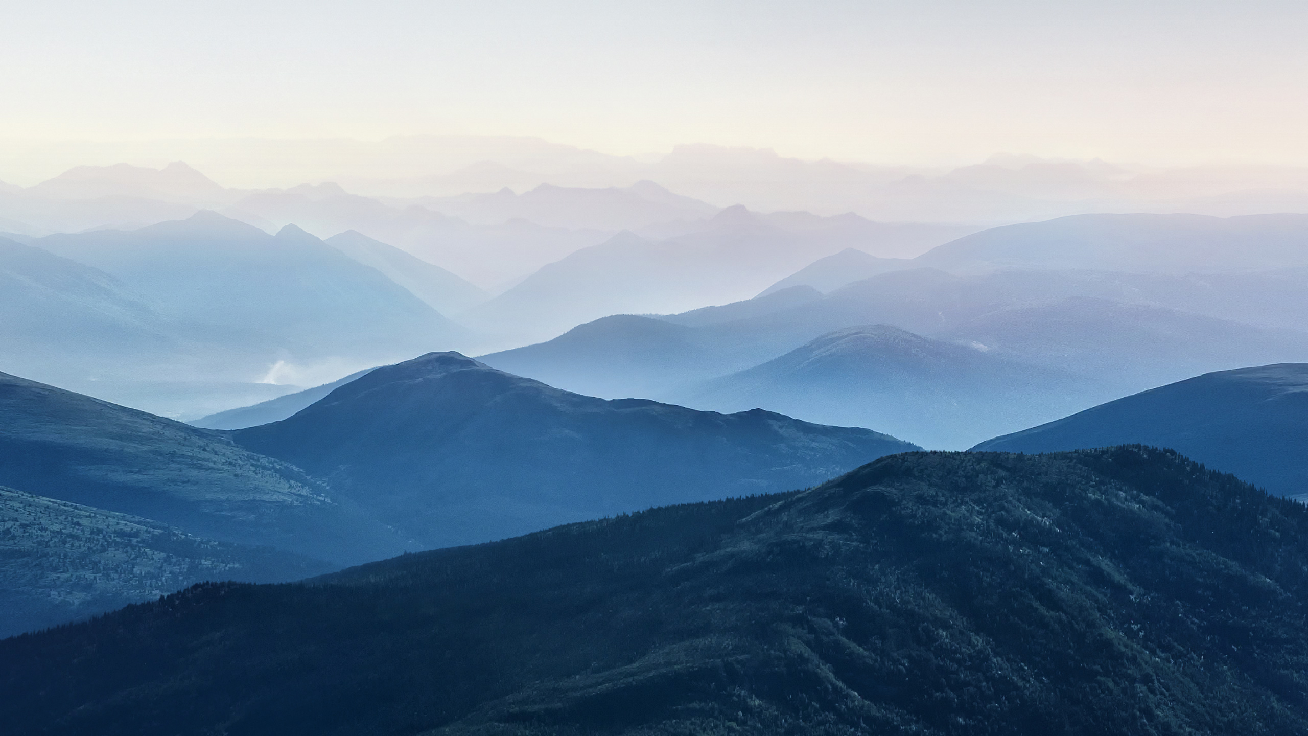 Layered blue mountains under a pale sky HD Wallpaper