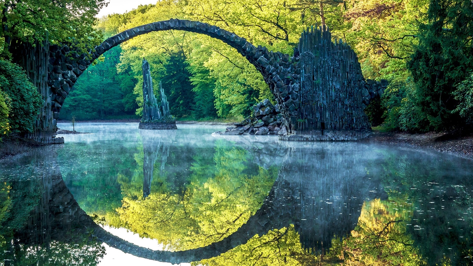 Stone arched bridge over a misty lake with reflections HD Wallpaper