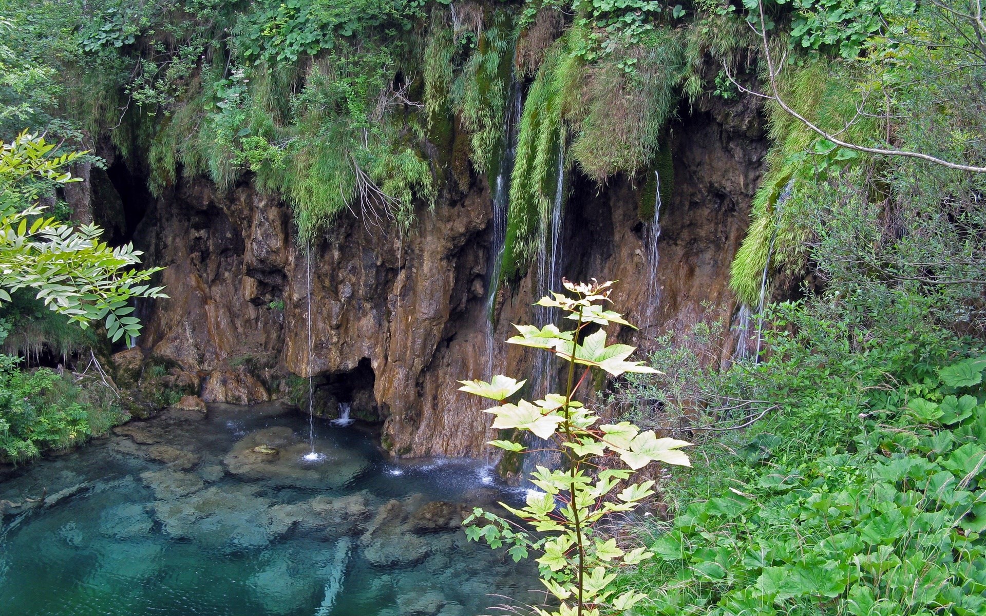 Waterfalls cascading into a clear turquoise pool in a rocky gorge HD Wallpaper