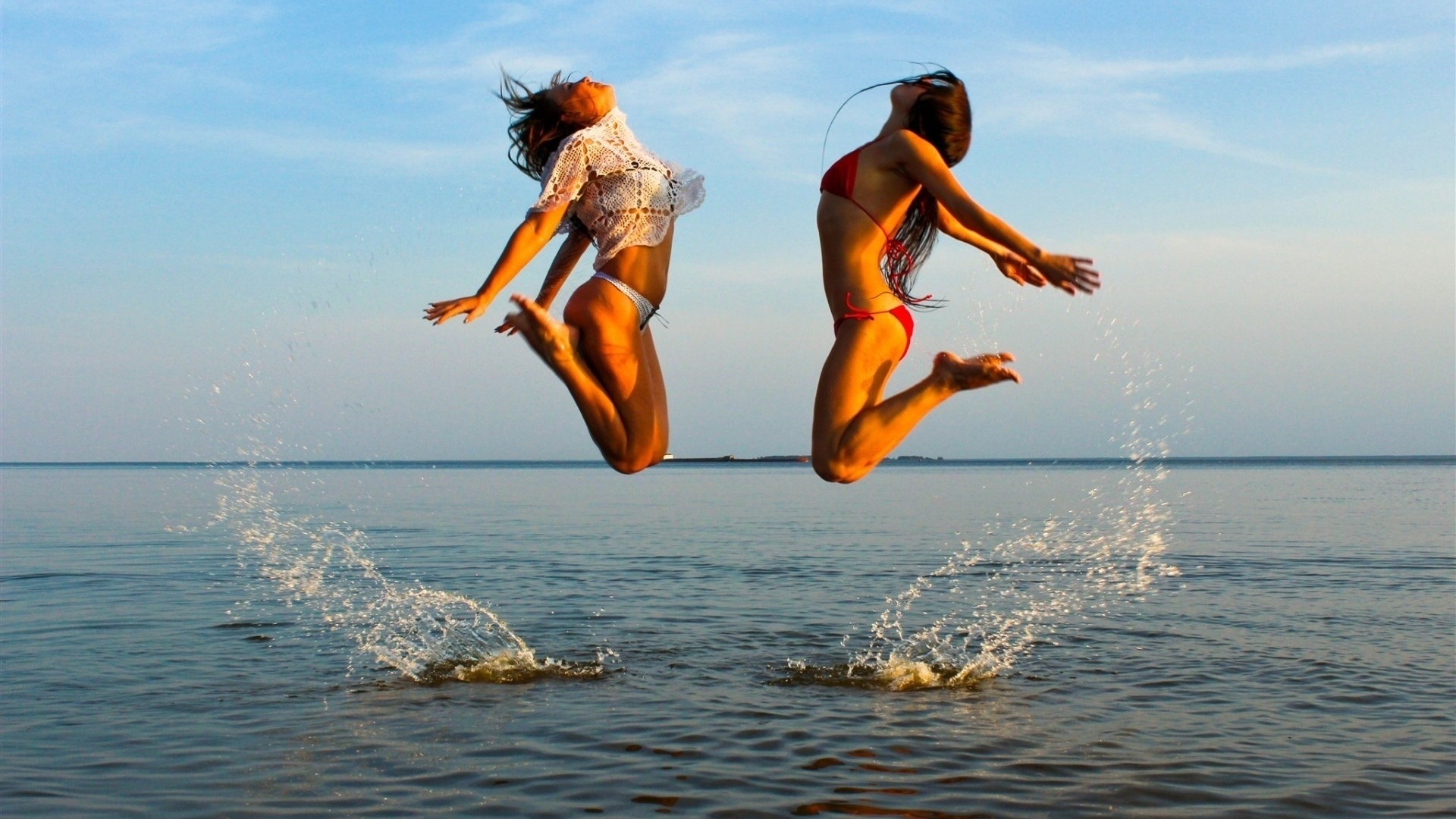 Two women jumping in the water HD Wallpaper