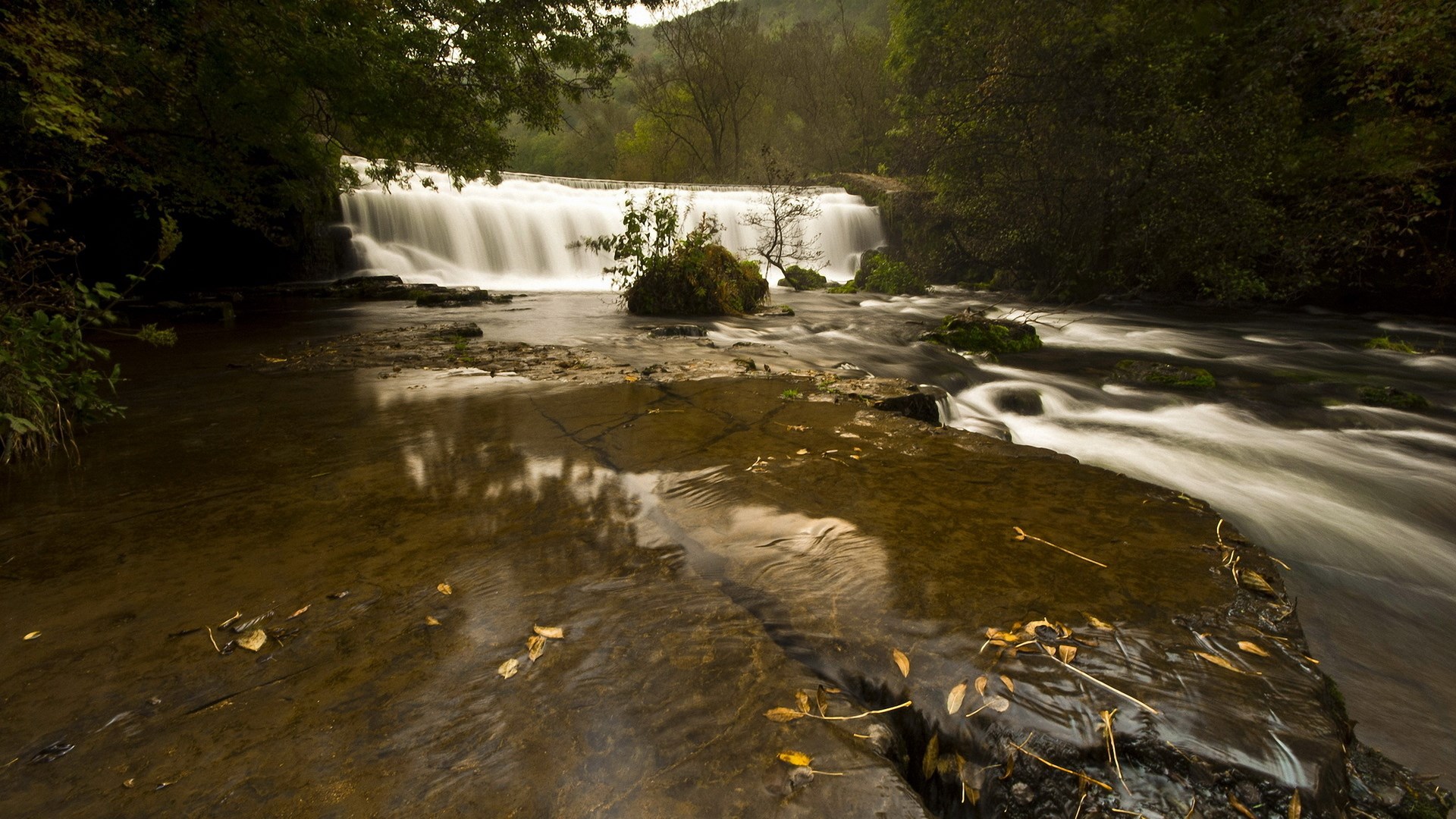 Waterfall flowing over rocks in a forest HD Wallpaper