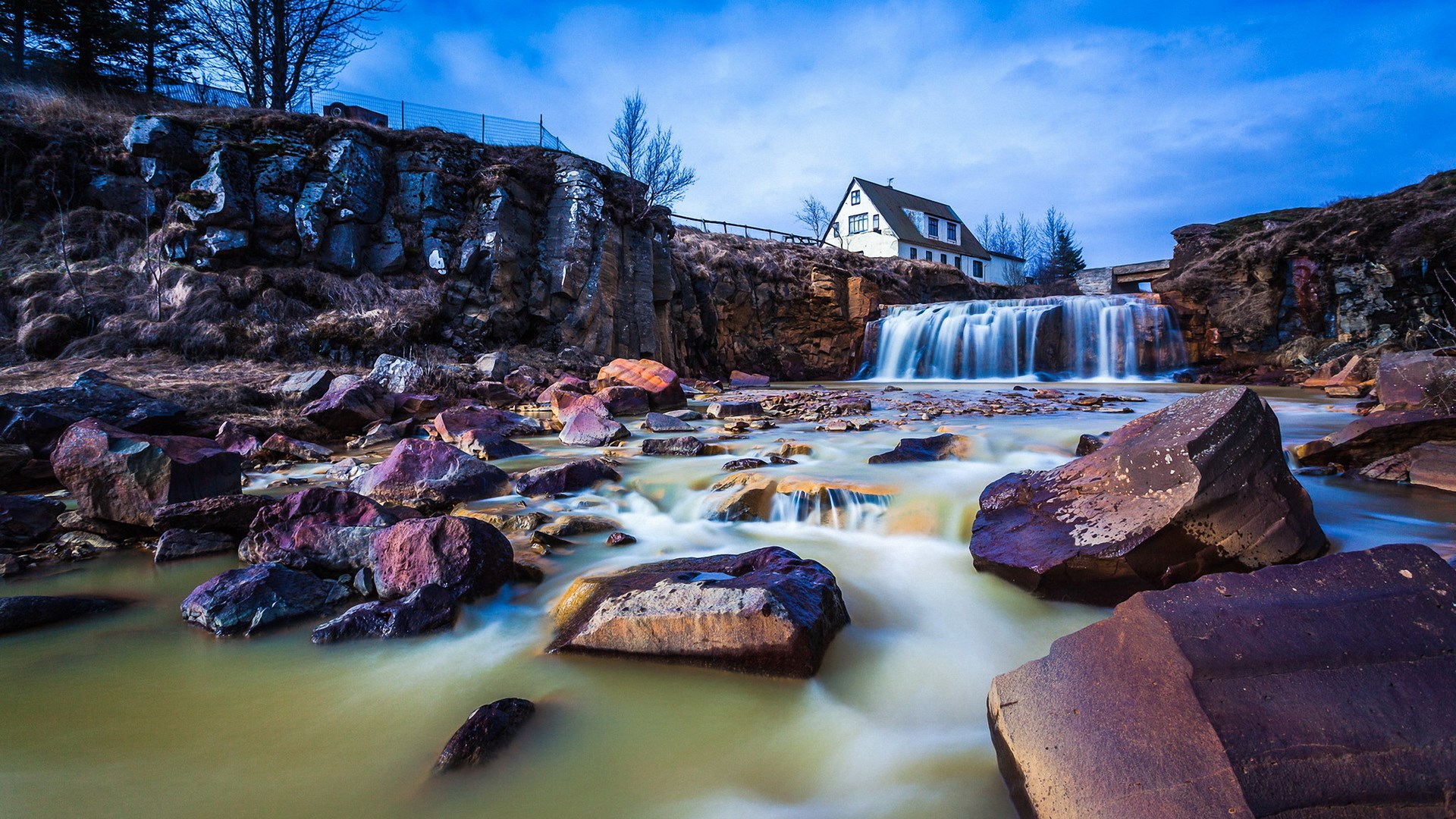 Waterfall near a white house on a rocky cliff HD Wallpaper