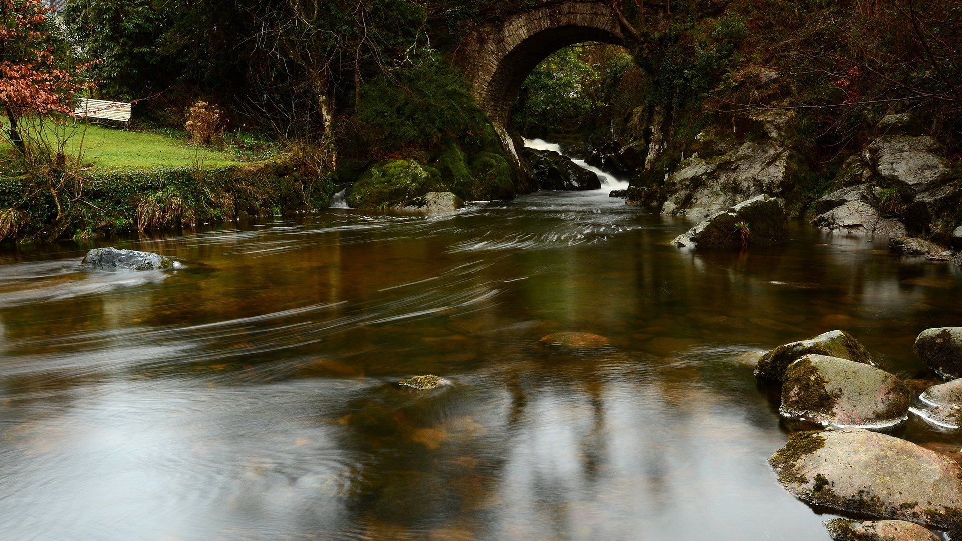 Stone bridge over a flowing river in a forest HD Wallpaper