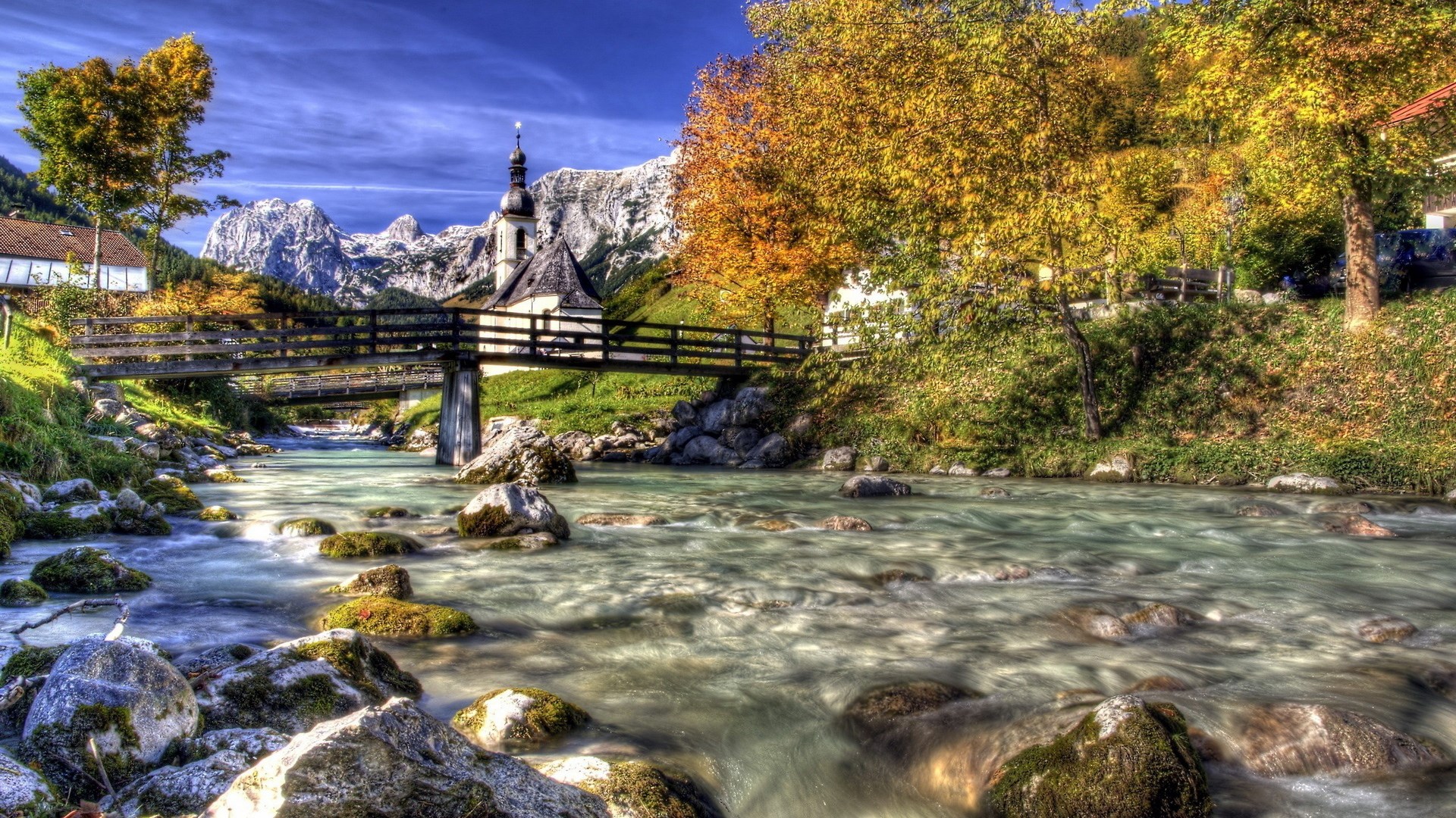 Wooden bridge over a river with a church and mountains HD Wallpaper