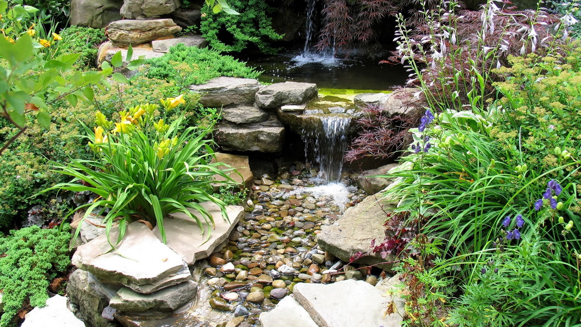 A tiered rock garden with a small waterfall and pond HD Wallpaper