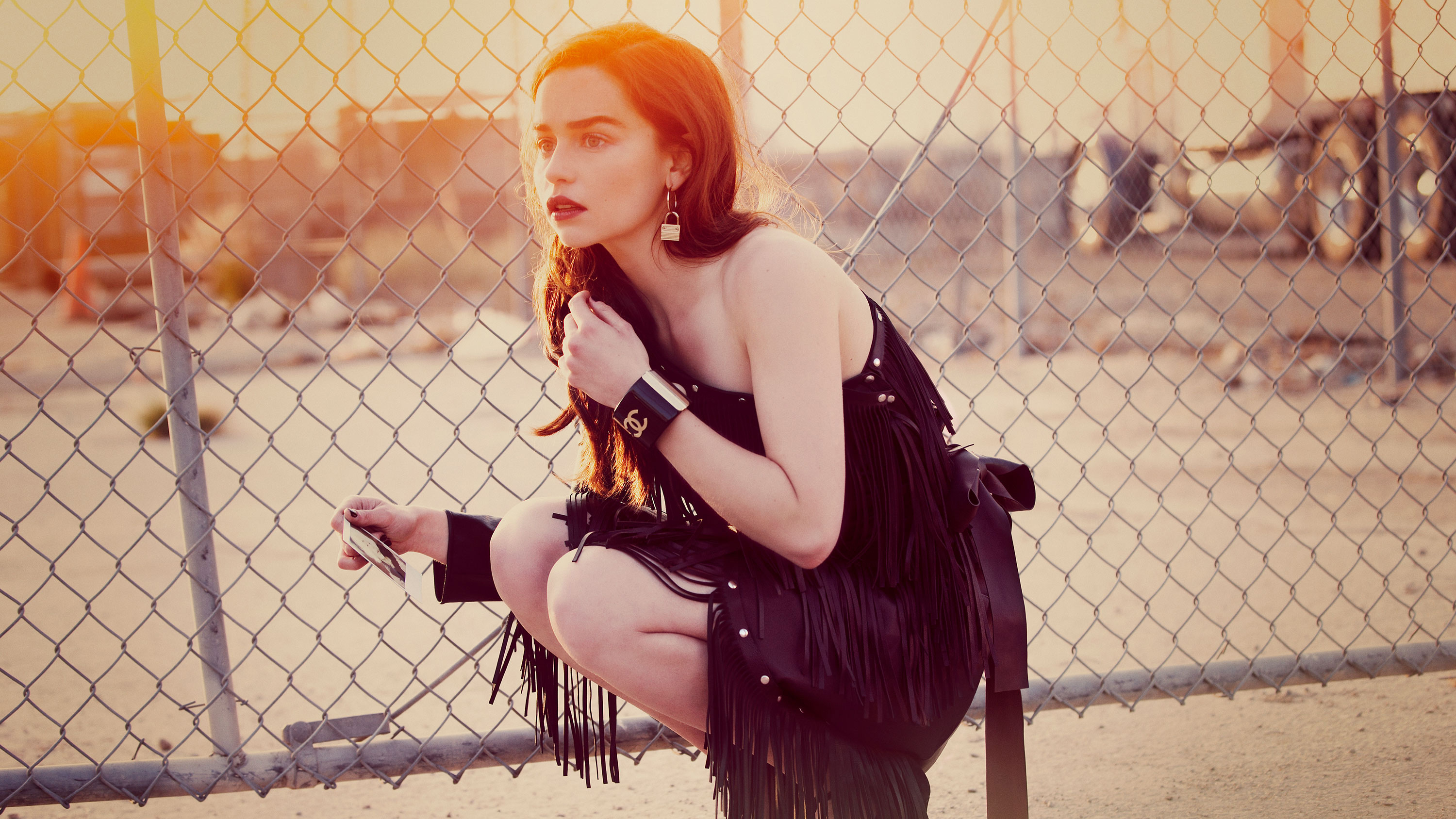 Emilia Clarke posing by a chain-link fence HD Wallpaper