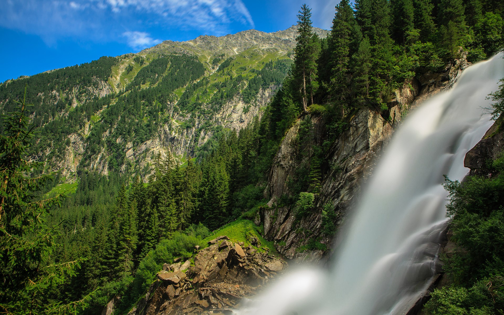 Waterfall cascading down a rocky mountain with pine trees HD Wallpaper