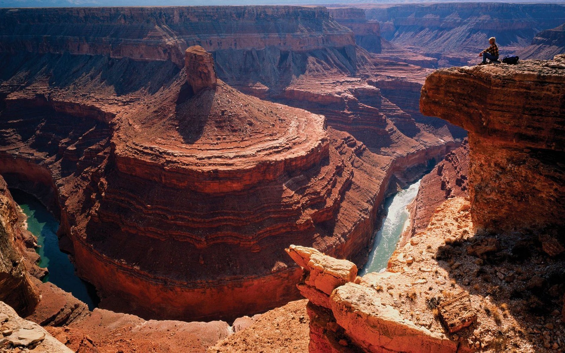 Person sitting on the edge of a canyon overlooking a river HD Wallpaper