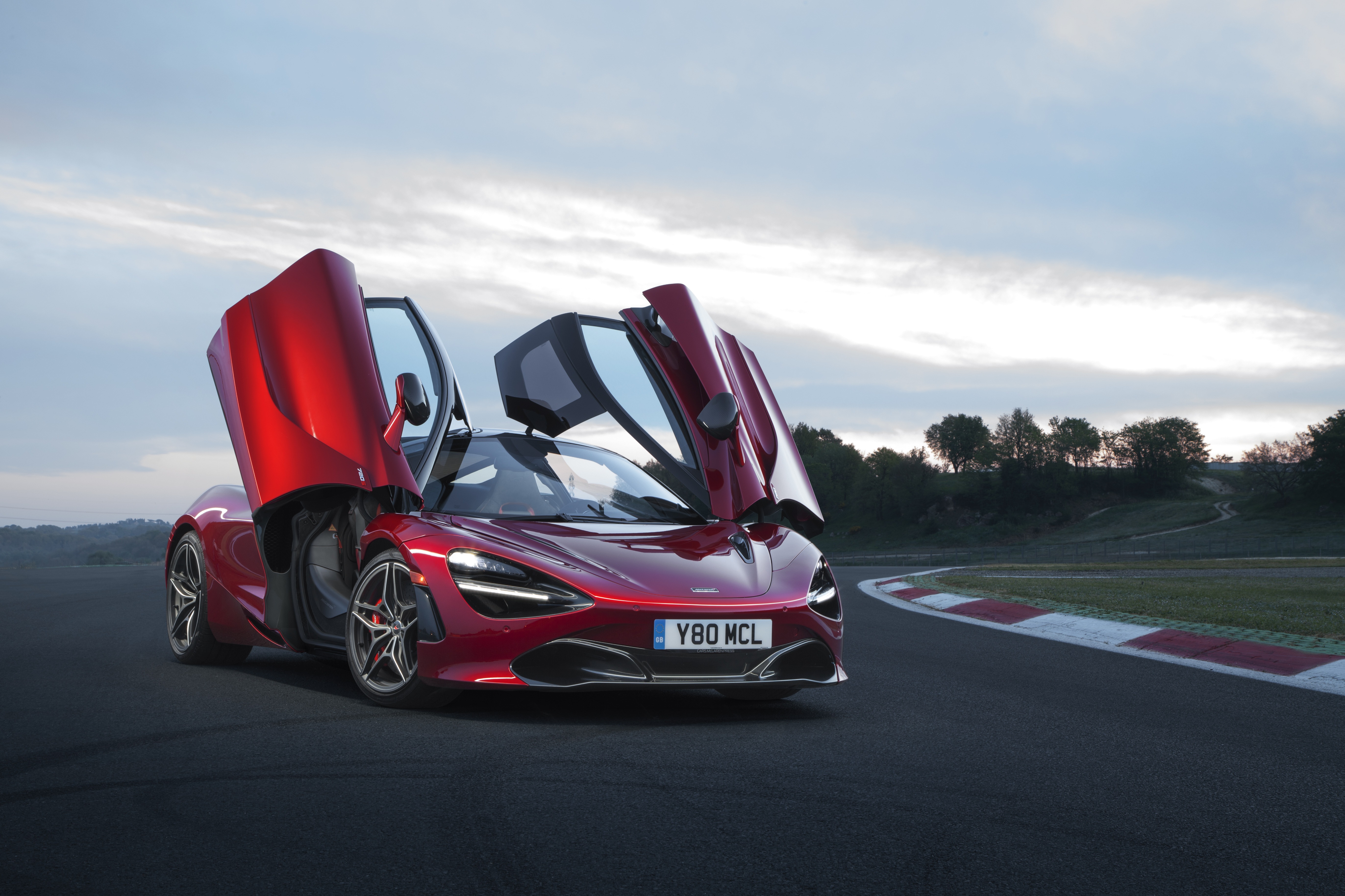 Red McLaren 720S with doors open on a race track HD Wallpaper