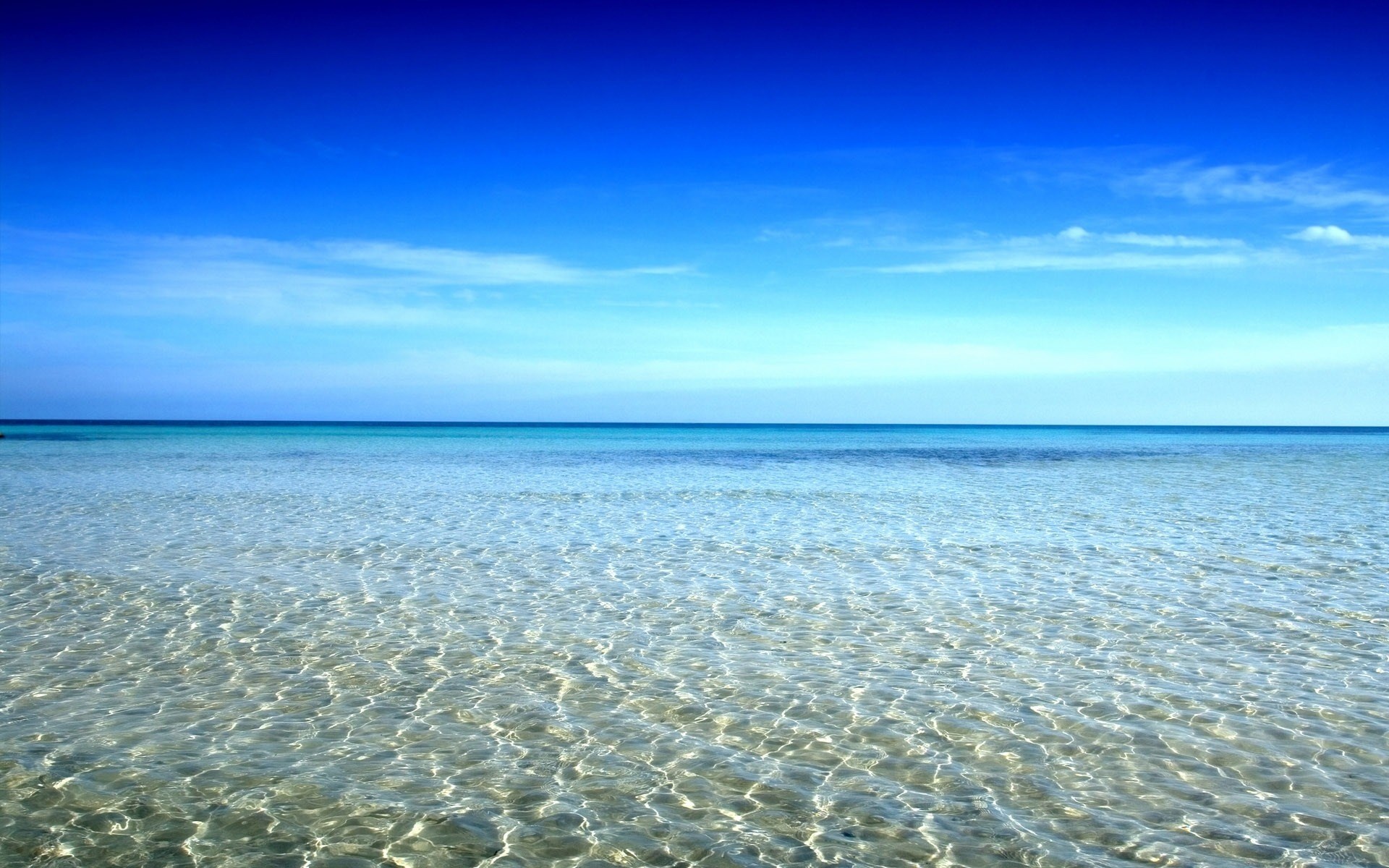 Crystal clear ocean water under a bright blue sky HD Wallpaper
