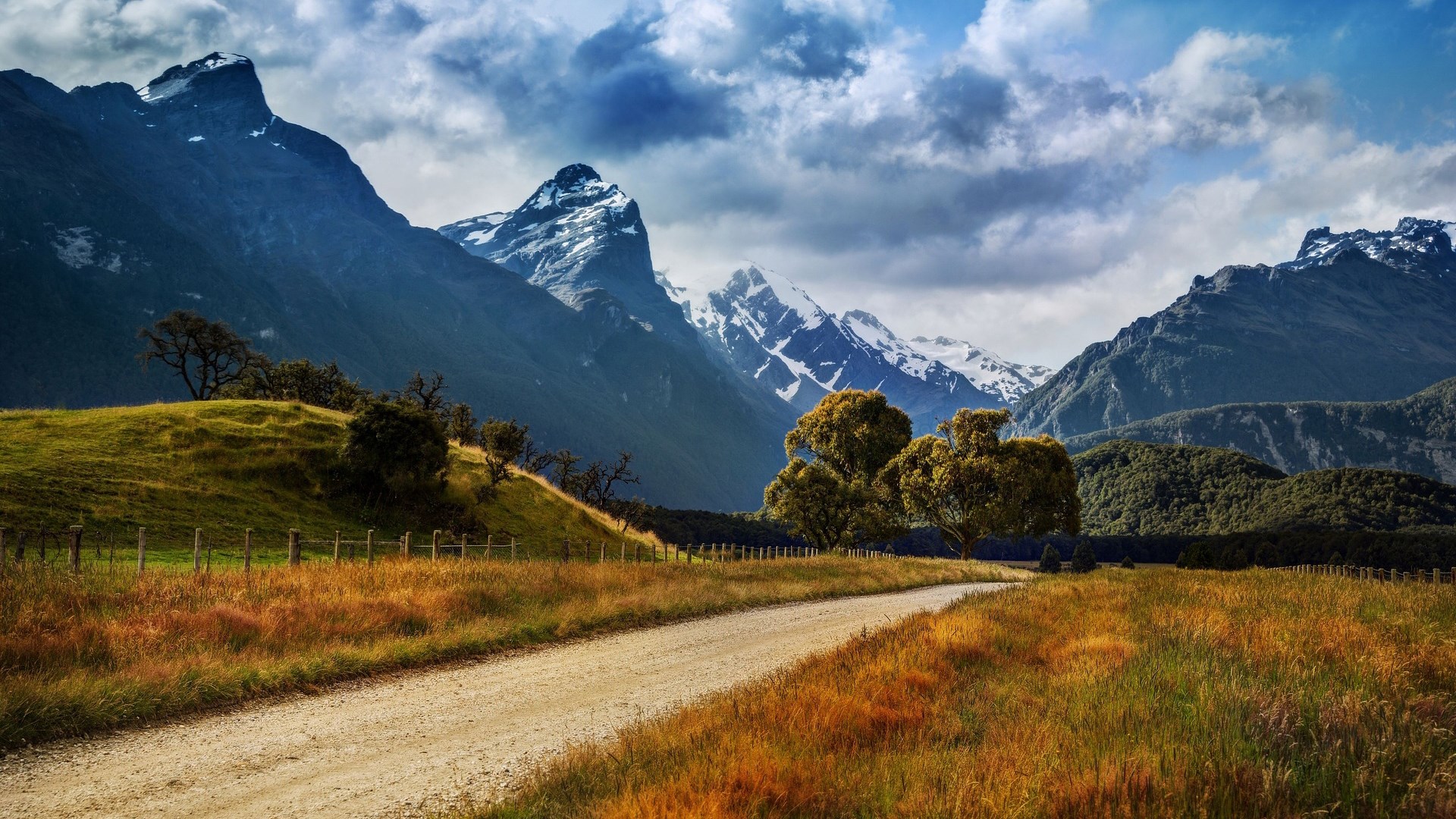 Dirt road through a grassy field with mountains HD Wallpaper